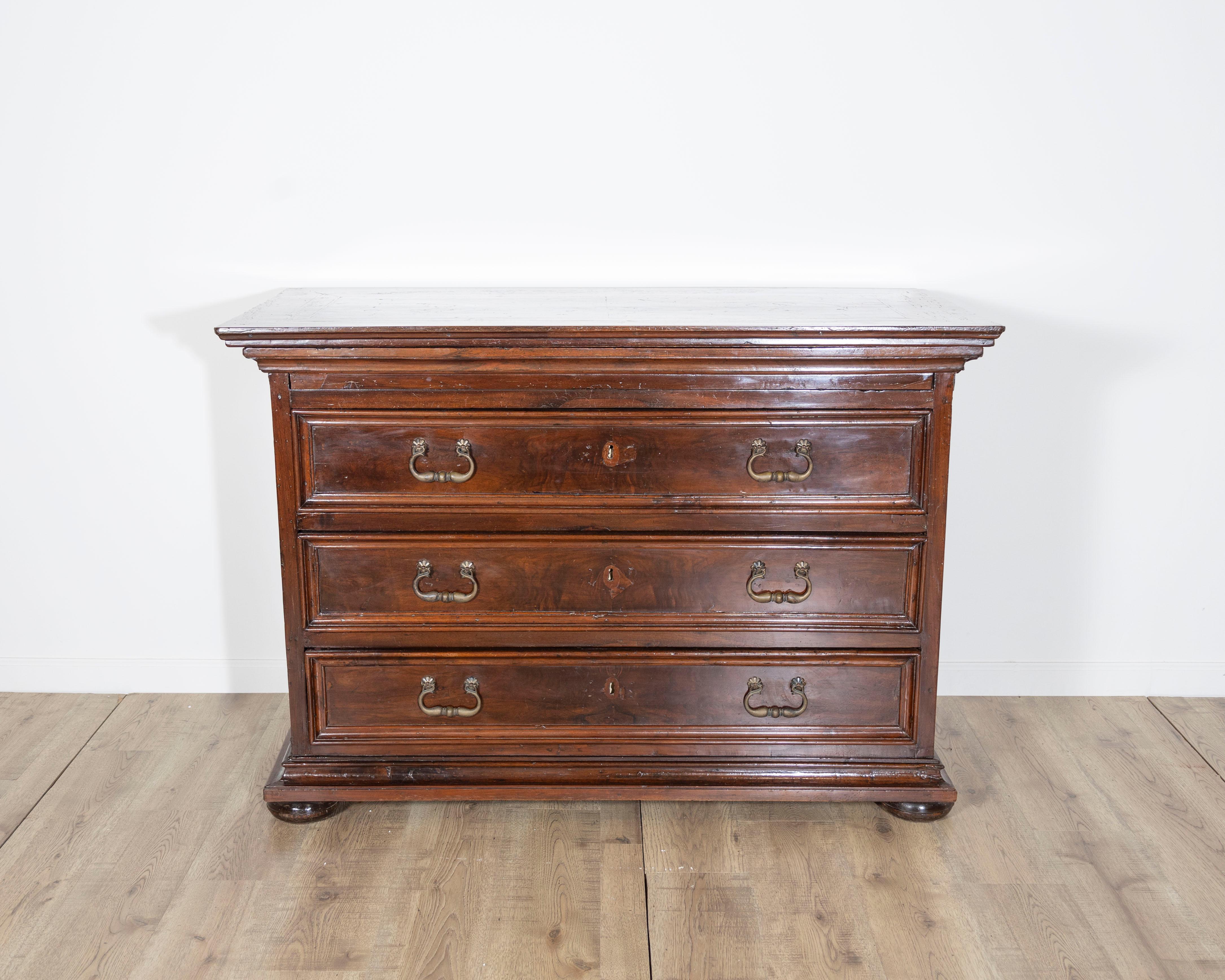 Cette impressionnante commode en noyer, datant de la fin du XVIIIe ou du début du XIXe siècle, reflète la solidité et l'élégance caractéristiques des meubles vénitiens anciens. Fabriquée en noyer richement patiné, cette pièce comporte trois grands