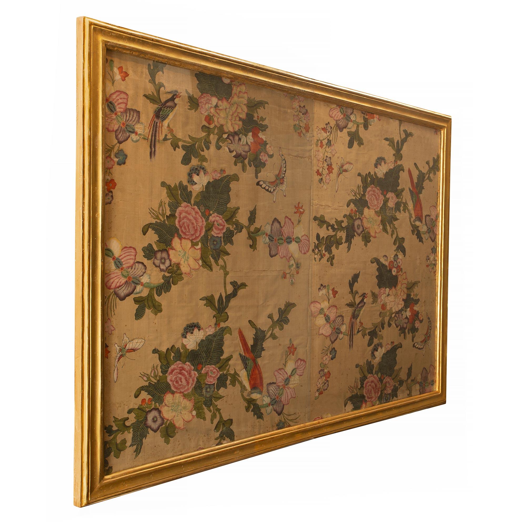 A most elegant 18th-century wall panel of hand-painted Asian silk of colorful branches filled with exotic flowers amidst birds and butterflies. The panel is fitted within an Italian 18th-century rectangular mottled giltwood frame from the Piedmont