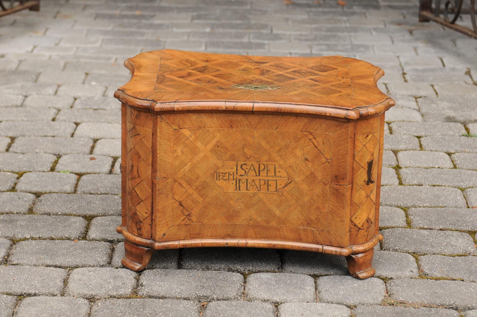 A continental walnut box from the mid-18th century with marquetry décor, inlaid boot motif, inscriptions and date. Born during the Rococo period, this exquisite petite box on feet features a diamond-shaped marquetry present on the lid and side