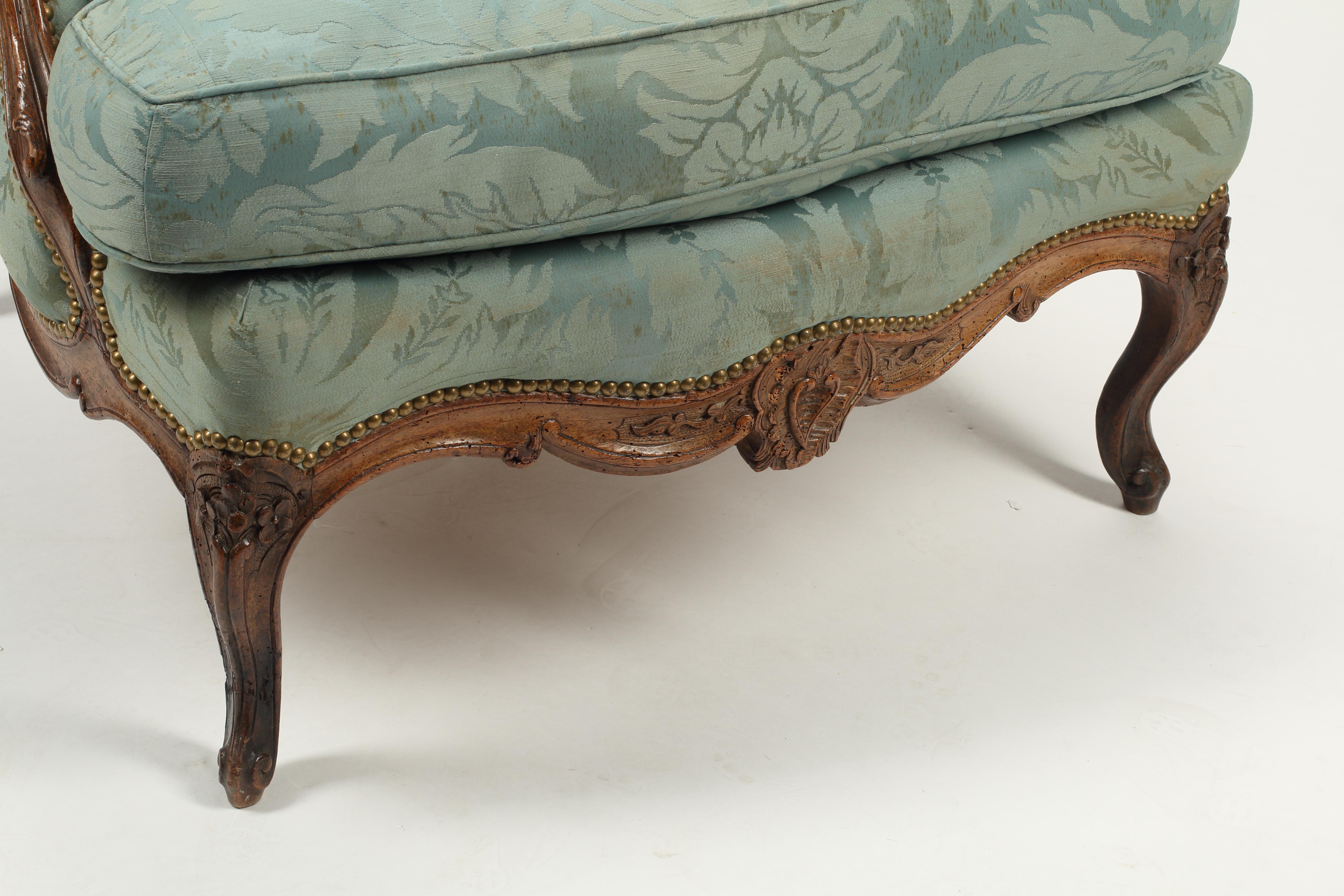 Cette bergère en noyer français du XVIIIe siècle est un exemple stupéfiant de l'artisanat et de l'art de cette période. La chaise provinciale française est fabriquée en noyer massif et présente des détails délicieusement sculptés, notamment un