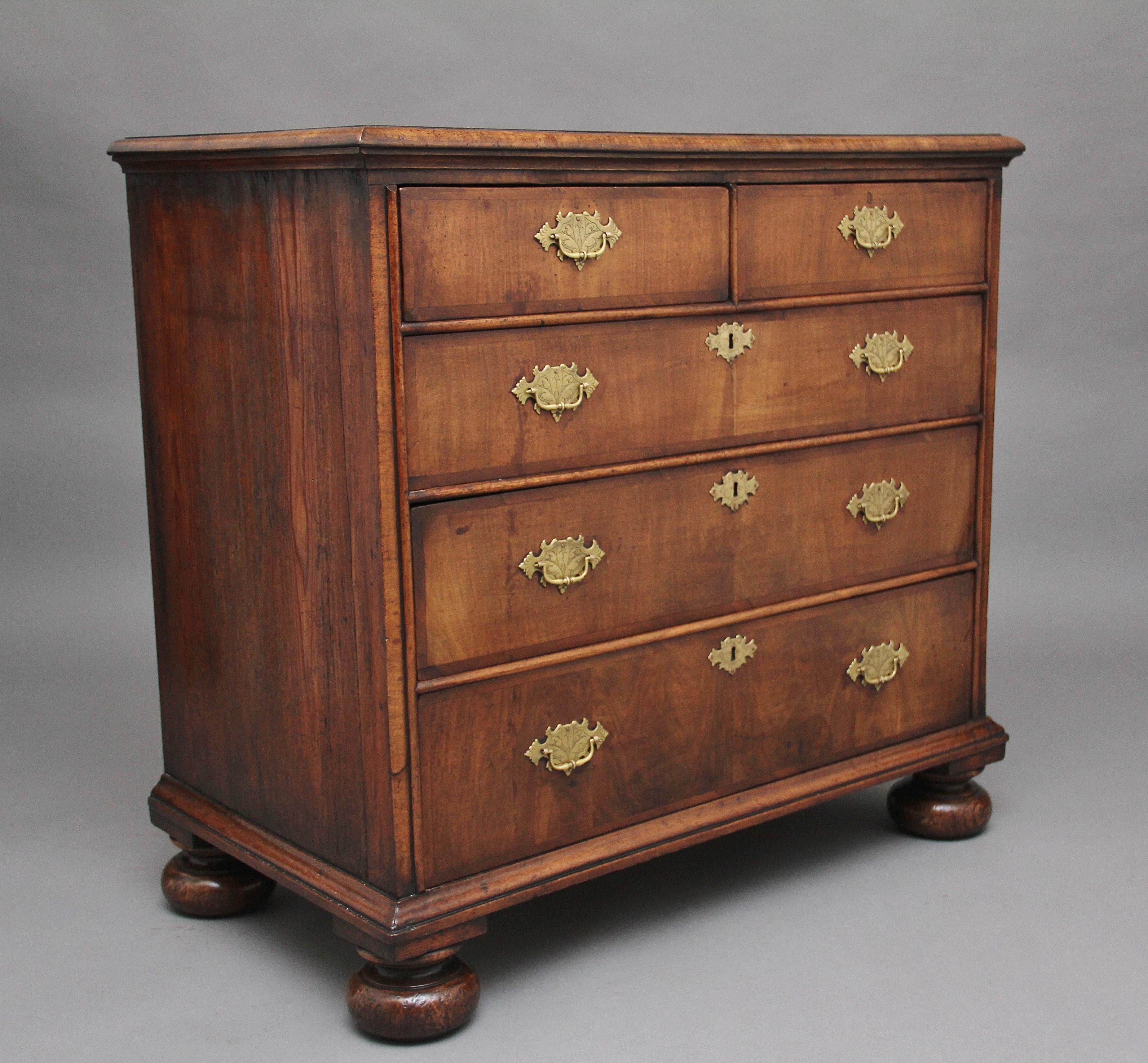 18th century walnut chest of drawers, the feather-banded and crossbanded rectangular moulded edge top over two short and three graduated long conforming drawers with brass engraved plate handles and escutcheons, standing on turned bun feet, circa