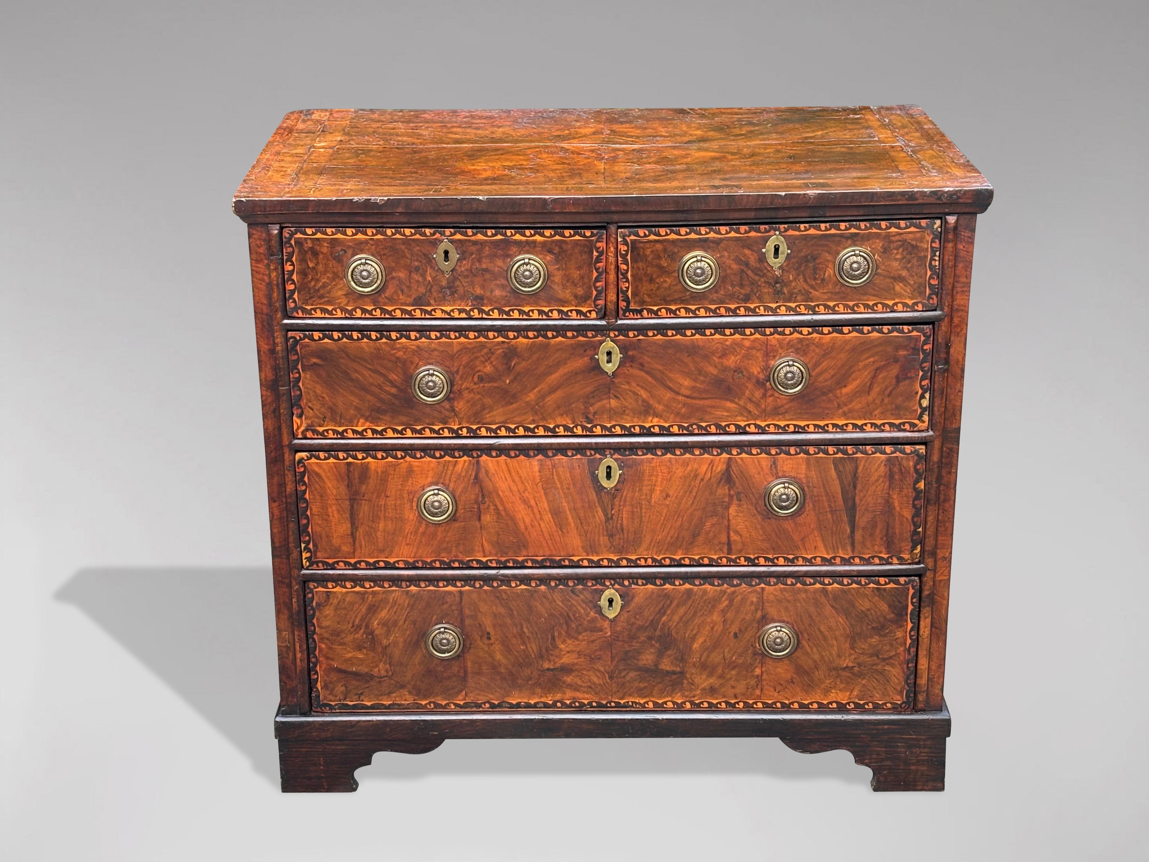 An 18th century country walnut chest of drawers. Walnut quarter veneers and crossbanding decorating the rectangular top, above two short over three long graduated marquetry banded oak lined drawers with quality brass ring handles, all supported by