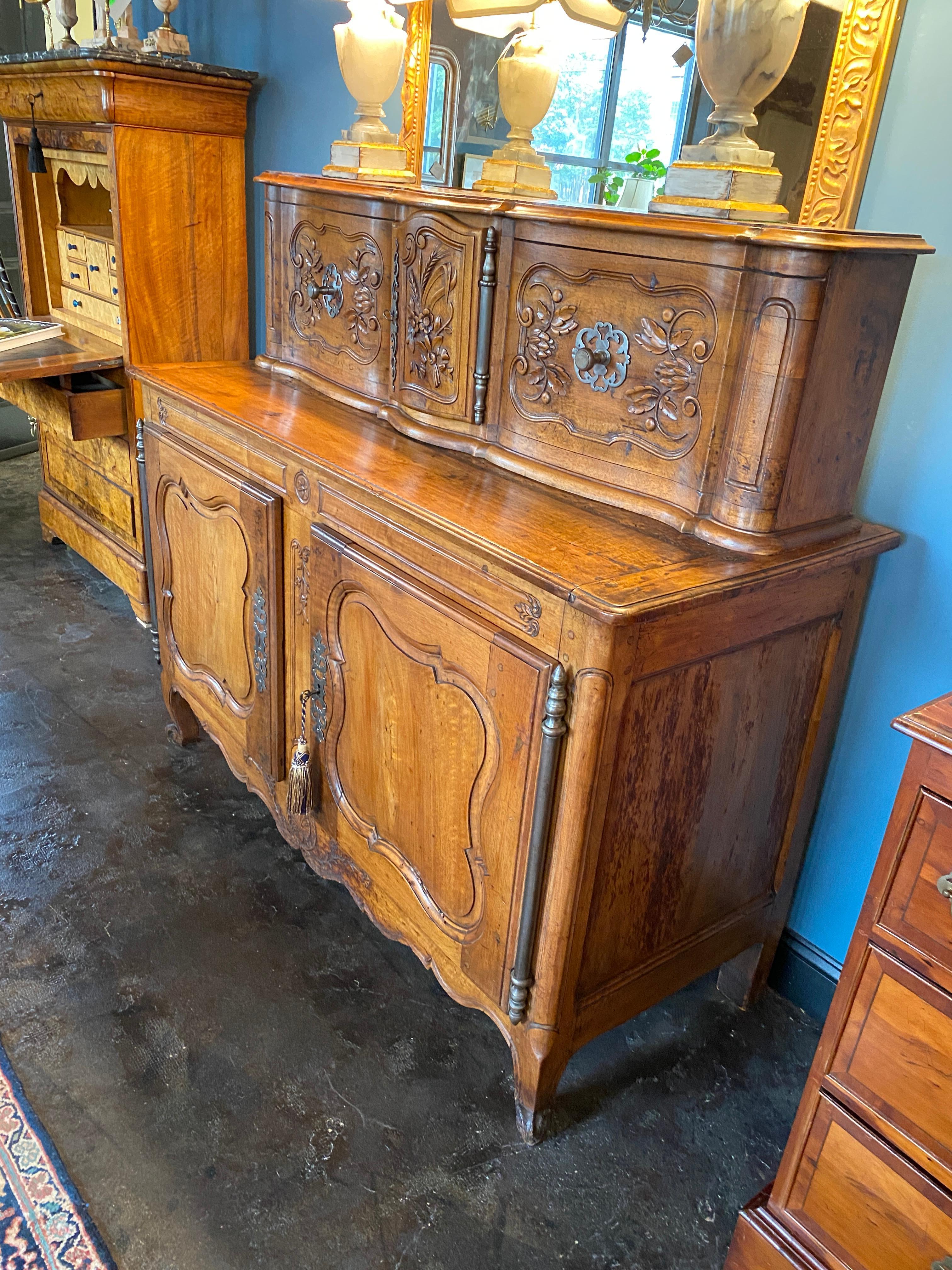 Handsome walnut buffet cabinet with hutch top. Two carved sliding doors and one central carved door with steel hardware. Carved Walnut door panels on the lower cabinet, fitted with one interior shelf and resting on cabriolet feets. Fantastic patina