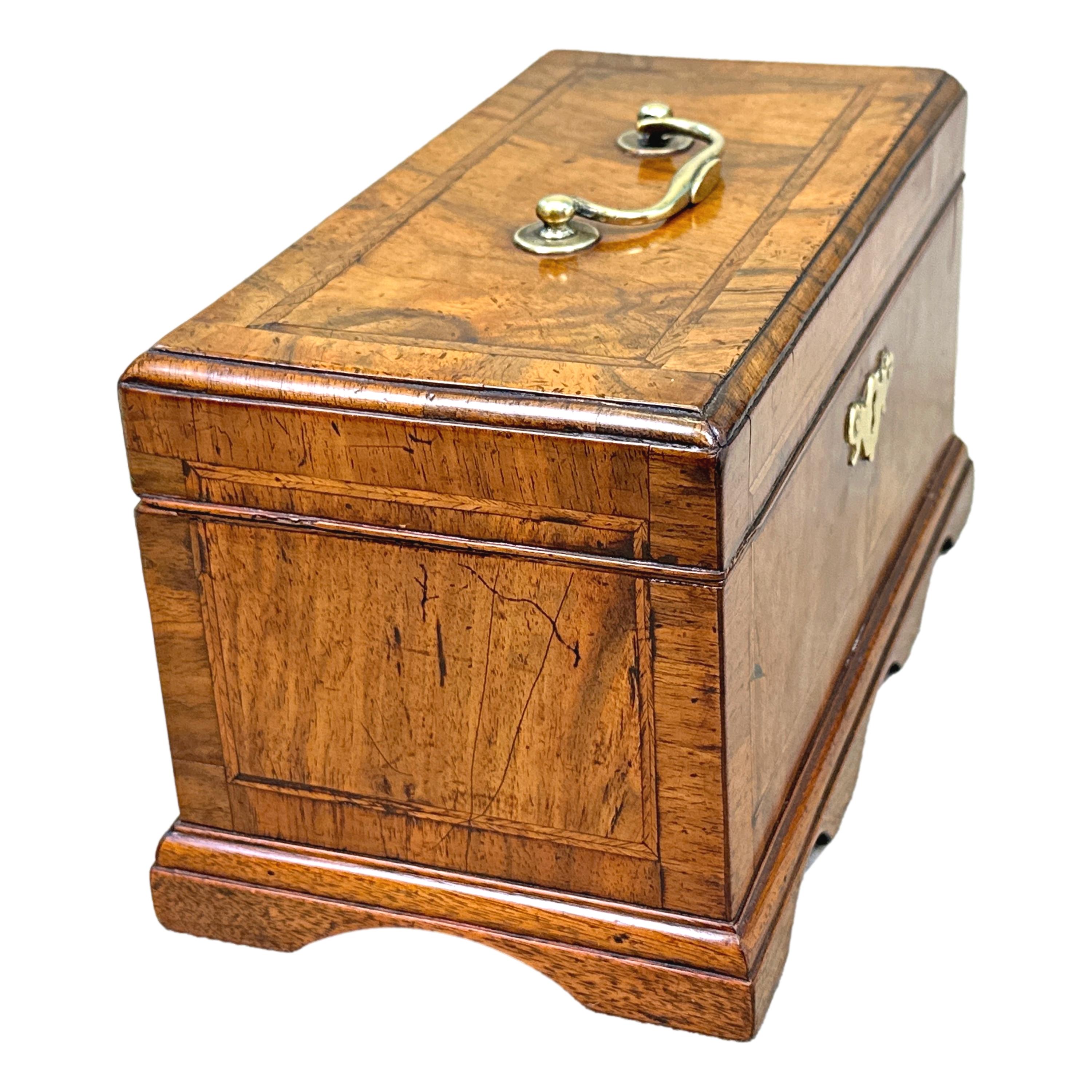 An Attractive Early 18th Century George II Period Walnut Tea Caddy Of Rectangular Form, Having Crossbanded And Inlaid Decoration To Top Enclosing Three Divisions, With Original Brasswear And Raised On Elegant Original Shaped Bracket Plinth.


A