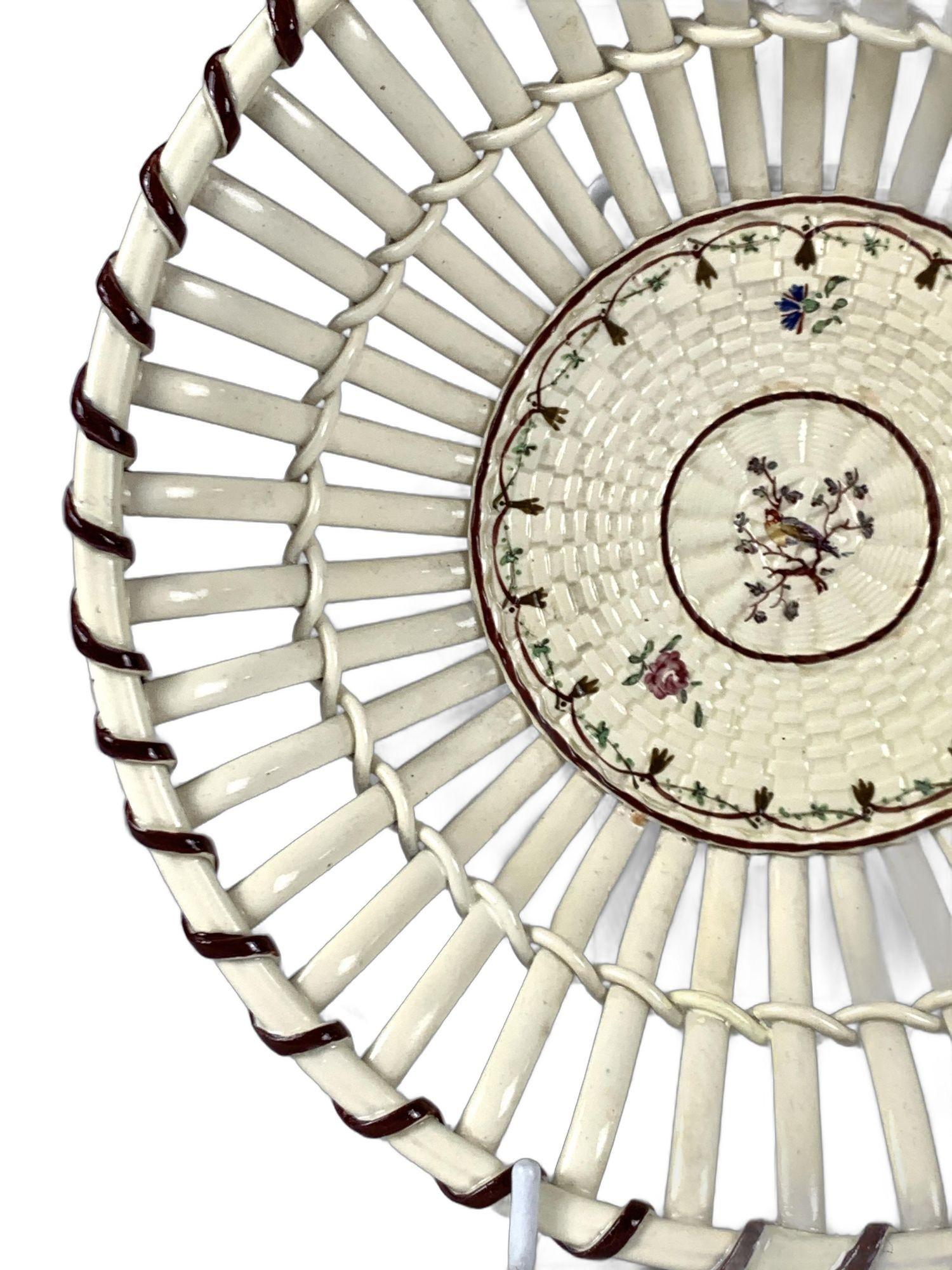 This delicate 18th-century Wedgwood creamware bowl features a hand-painted songbird at its center.
It is a masterpiece of craftsmanship.
The bowl is made from fine, pale, cream-colored creamware.
Its intricate openwork strap design allows light to