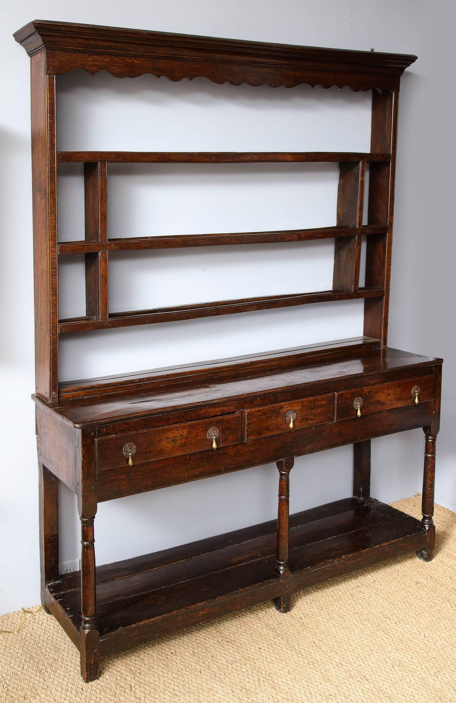 Fine 18th century English or welsh oak dresser, having richly molded crest over scalloped fascia, the divided shelves with plate grooves and standing on molded top over three drawers, the front legs with balustrade turnings, and standing on open