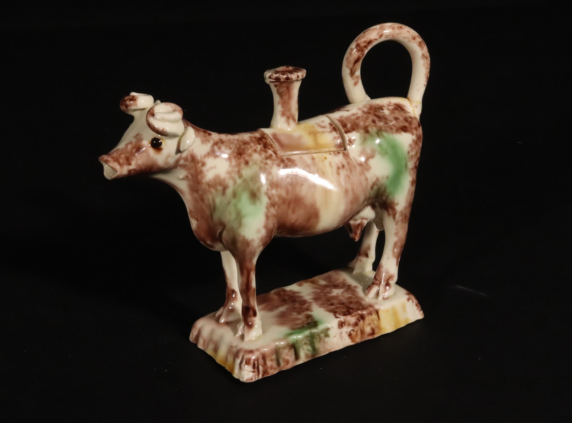 Crèmerie de type Whieldon  Crémier et couvercle pour vaches,
Circa 1770

L'attrayant crémier à vache et son couvercle, de type Whieldon, reposent sur une base rectangulaire à bord cannelé.  Le crémier et la base sont épongés en brun et vert avec une