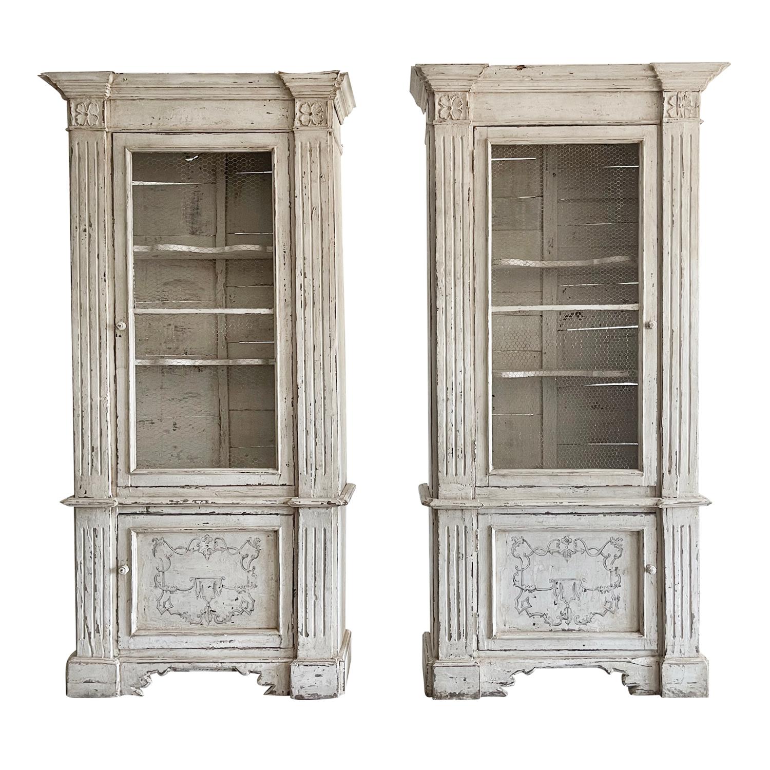 An antique distinctive pair of 18th century display cabinets with a tall crown molding, made of solid walnut, original hardware and painted interior, in good condition. The upper doors have the typical decorative mesh screen doors and three shelves