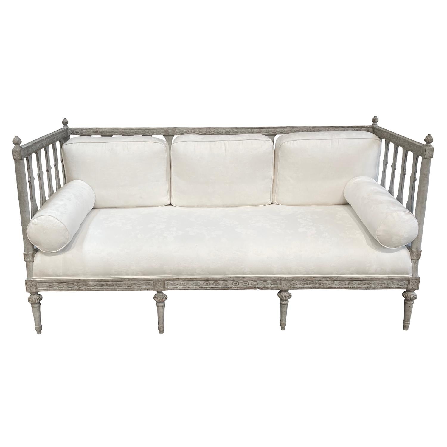 A white-grey, antique Swedish Gustavian sofa bench, daybed with three large back pillows and two round pillows, made of hand carved Pinewood, in good condition. The tall back, side rests of the Scandinavian wood bench is spindled, supported by
