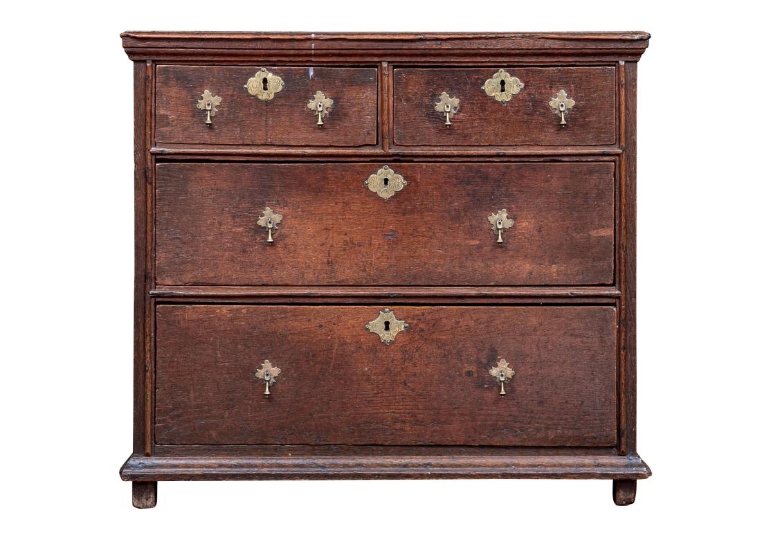 A handsome smaller chest in a Primitive rendition of the more refined William and Mary Style. This well made English Cabinet has the original incised brass drop-pulls and escutcheons with delicate incised floral decoration. Very well constructed