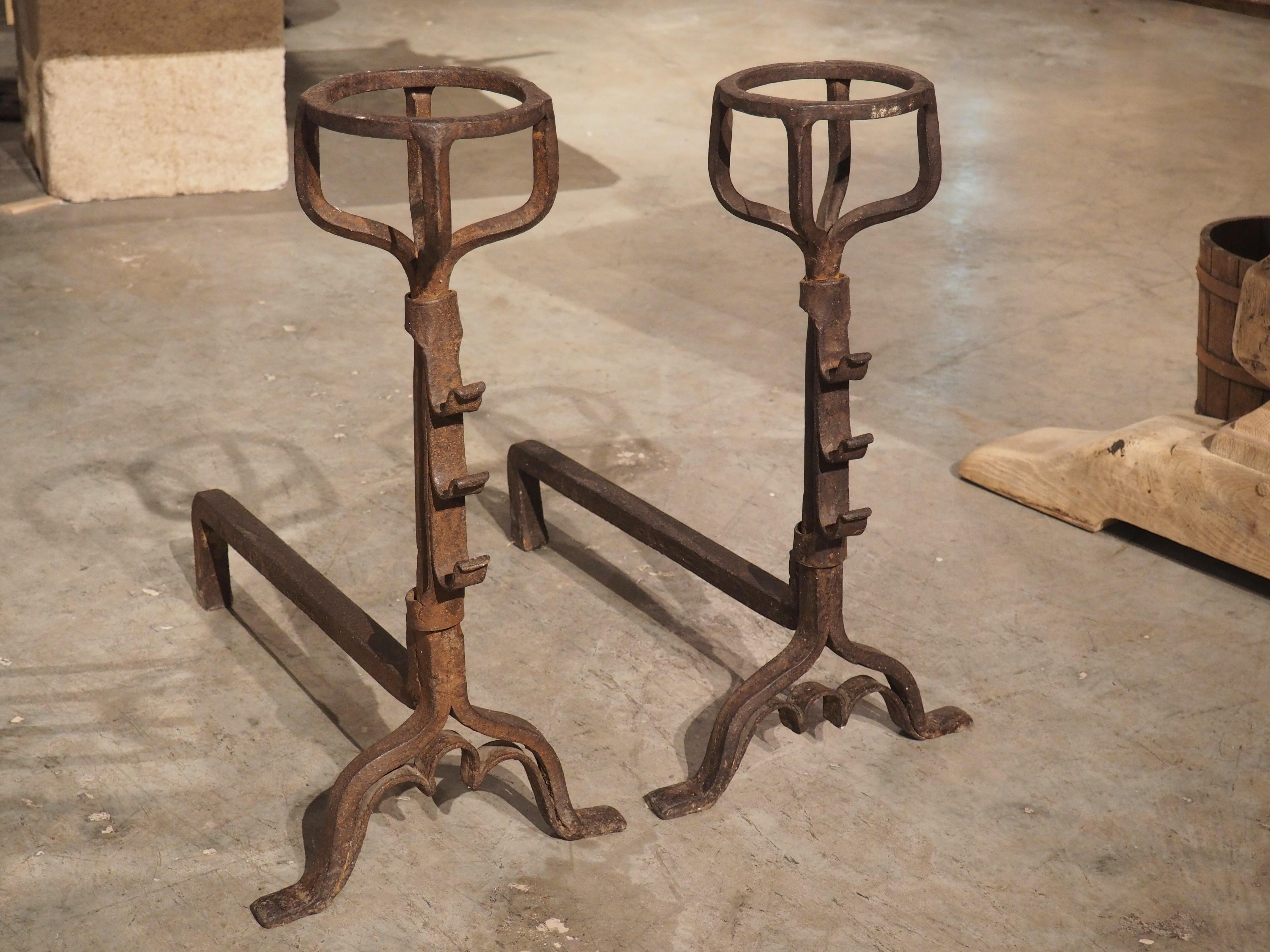 These antique French “chenets” are from the 1700s and have been hand-wrought in iron. Their uppermost portions were crafted to hold cups or bowls of liquid which would then be heated from the fire behind. The hooks attached to the front of the