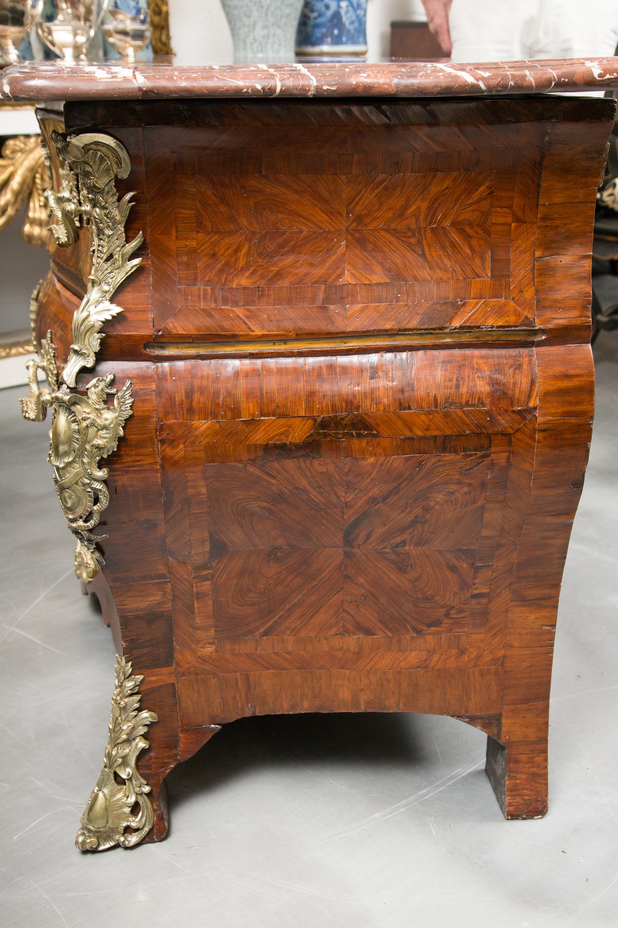 This is an impressive 18th century Louis XV Tulipwood and Kingwood commode with a rouge variegated marble top over three long graduated drawers and overall embellished with ornate gilt bronze metal mounts. On the top left corner of the commode is a