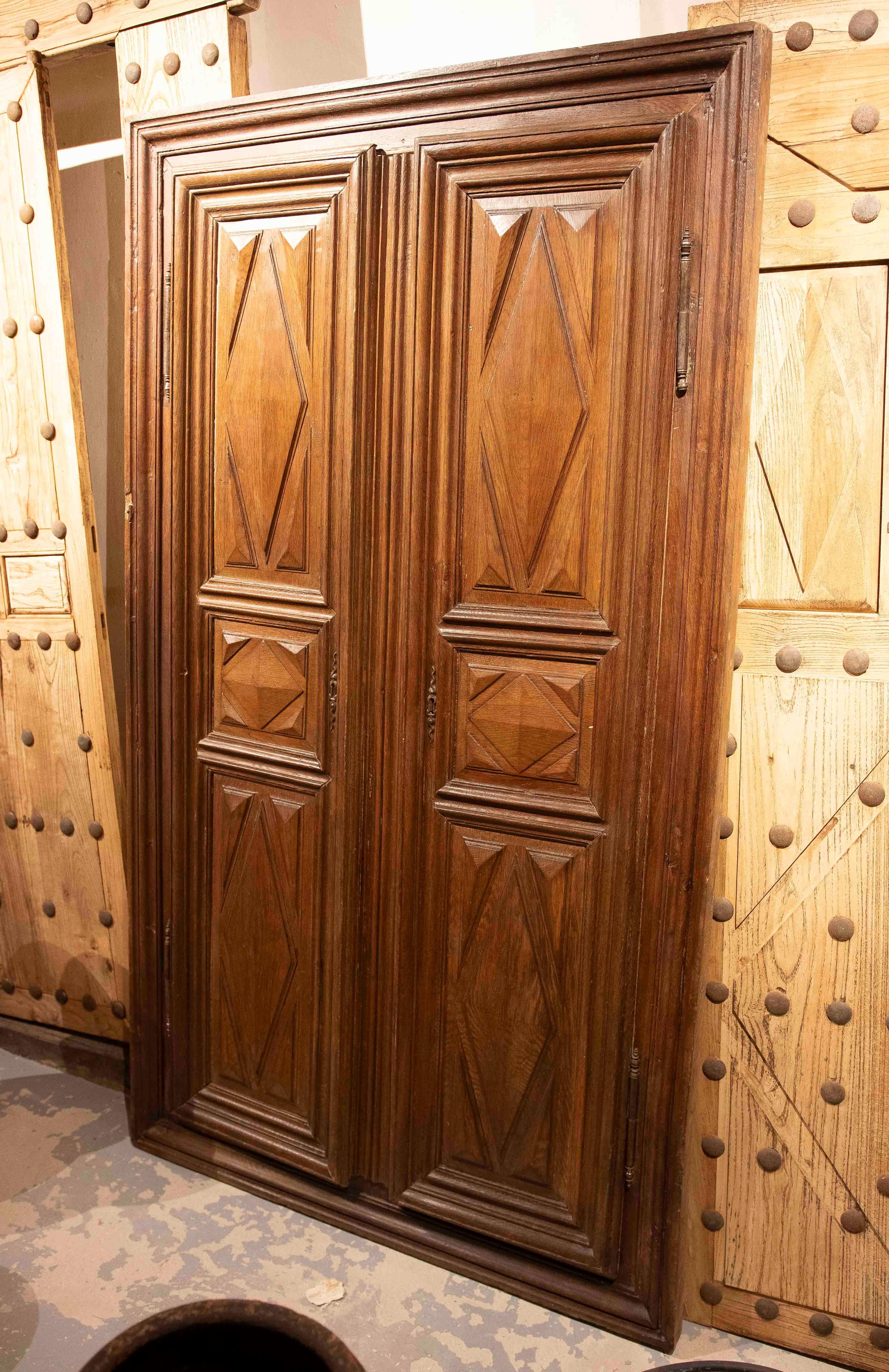 Antique double-leaf door made of solid wood, with a sober and elegant design characterized by panels framed with geometric carvings in the shape of rhombuses and diamonds. Each leaf features a symmetrical composition distributed in three registers,