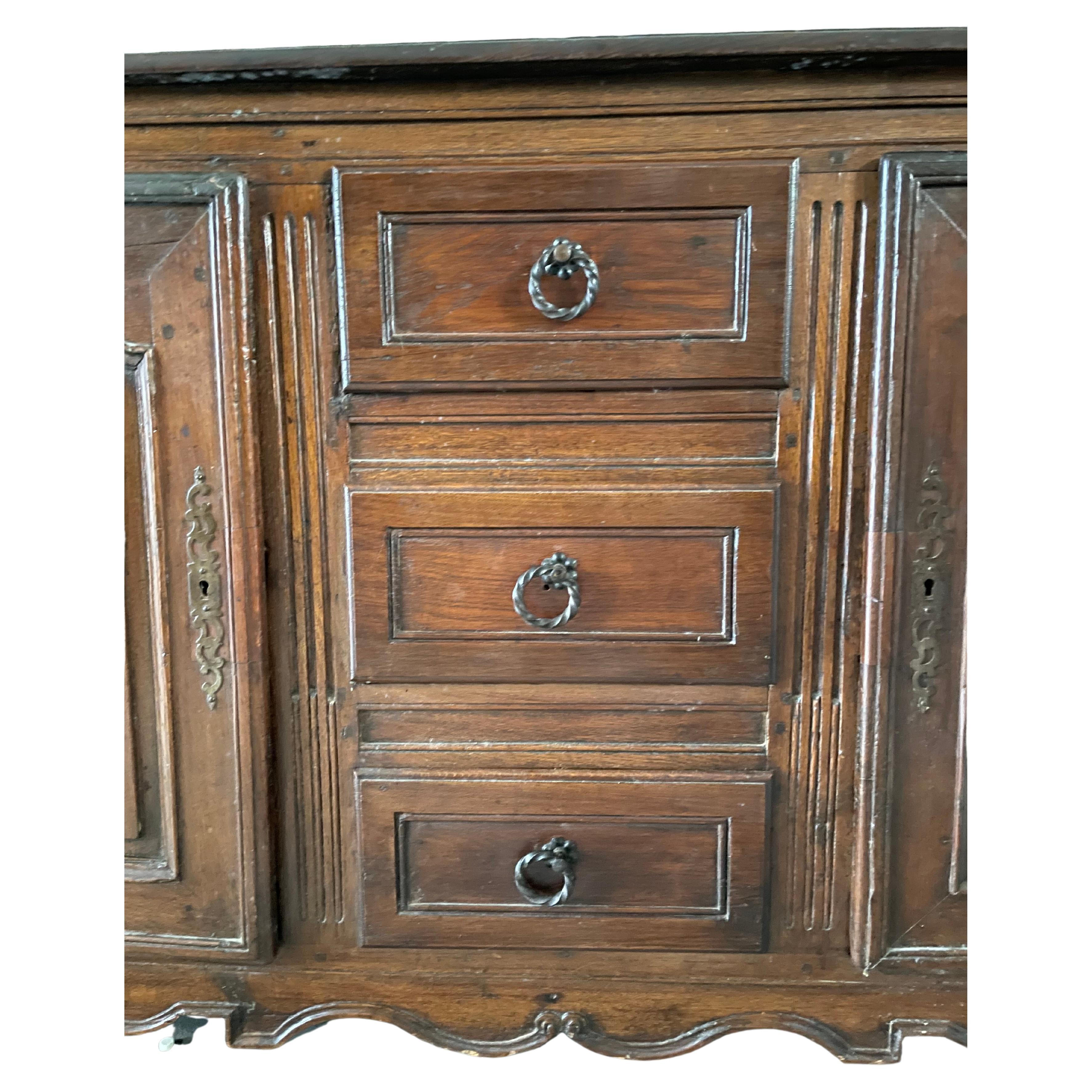 18th century French buffet in oak Louis XV
Two wide doors and 3
central drawers form the facade. Each door is sculpted in motion. The carved lower part gives a nice movement to the whole piece of furniture. The top is made of wood, the patina is