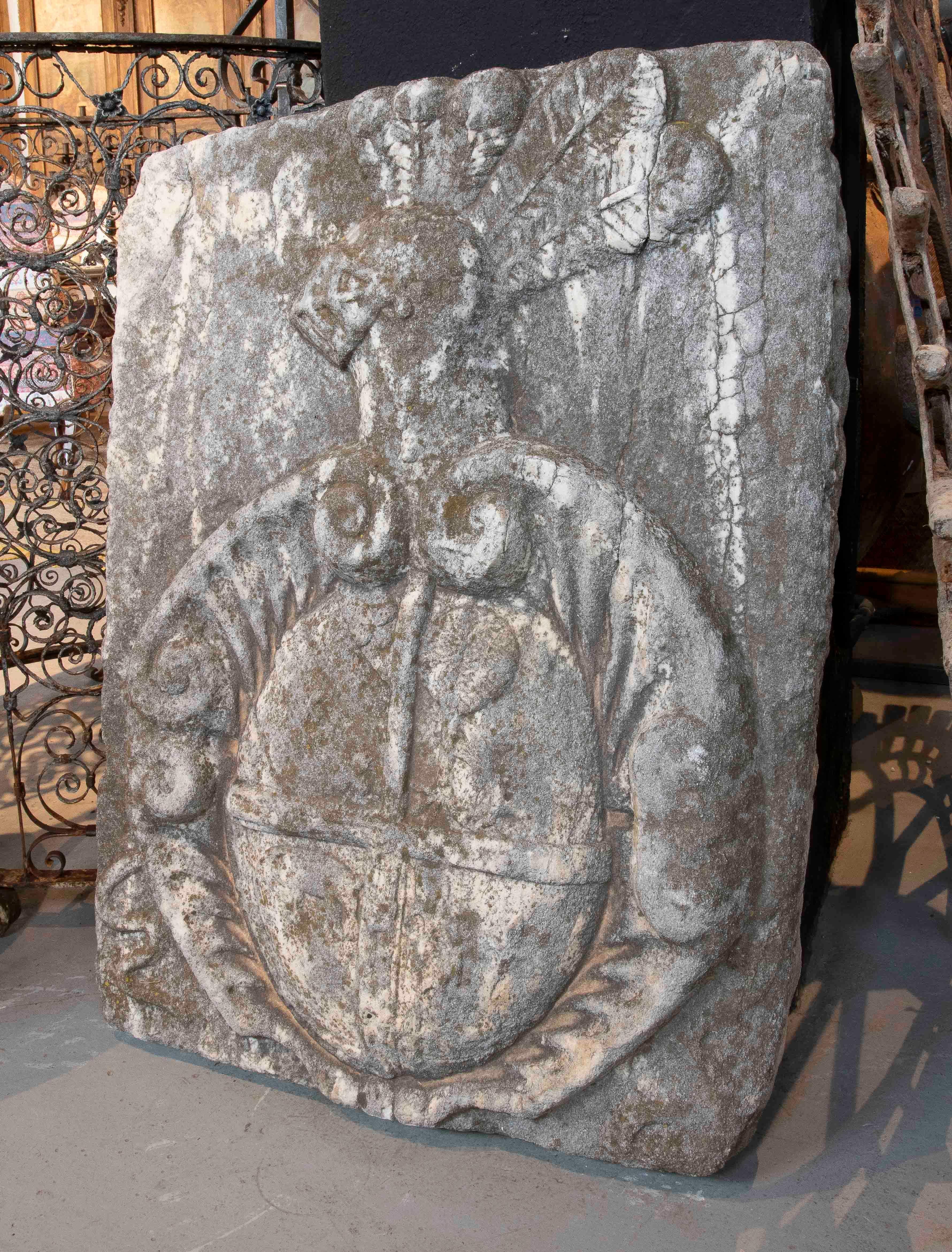 Imposantes, geschnitztes Steinschild mit heraldischem Motiv, das ein großes, in Viertel geteiltes Zentralschild zeigt, das von geprägten Akanthusblättern umgeben ist. Oben ist der Helm eines Ritters zu sehen, der mit einer Feder gekrönt ist, ein