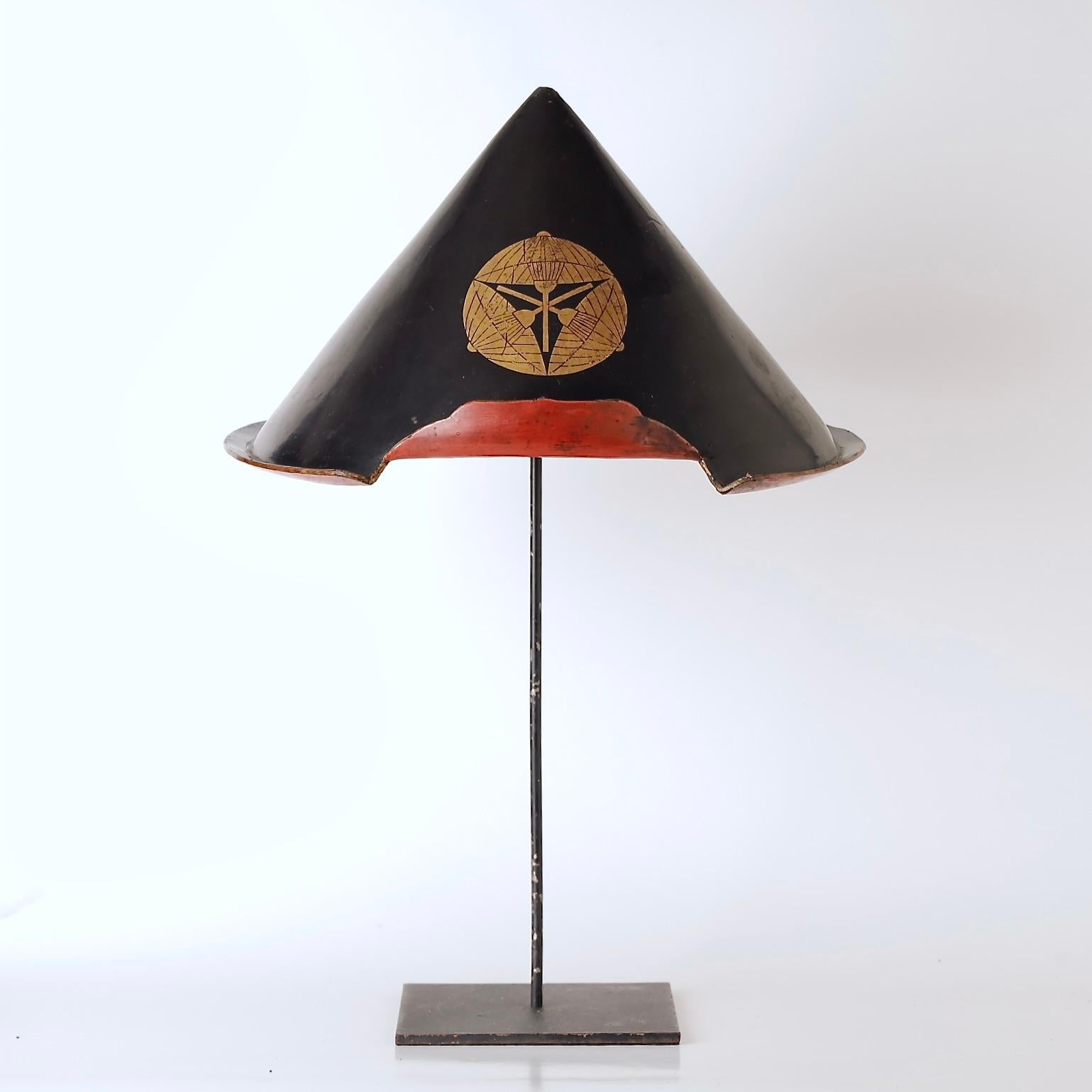 A rare and historically significant lacquered Jingasa—a domed hat worn by samurai and their retainers—dating to the mid-Edo period (18th century). This lightweight wood hat is finished in deep black lacquer and features a boldly rendered gold clan