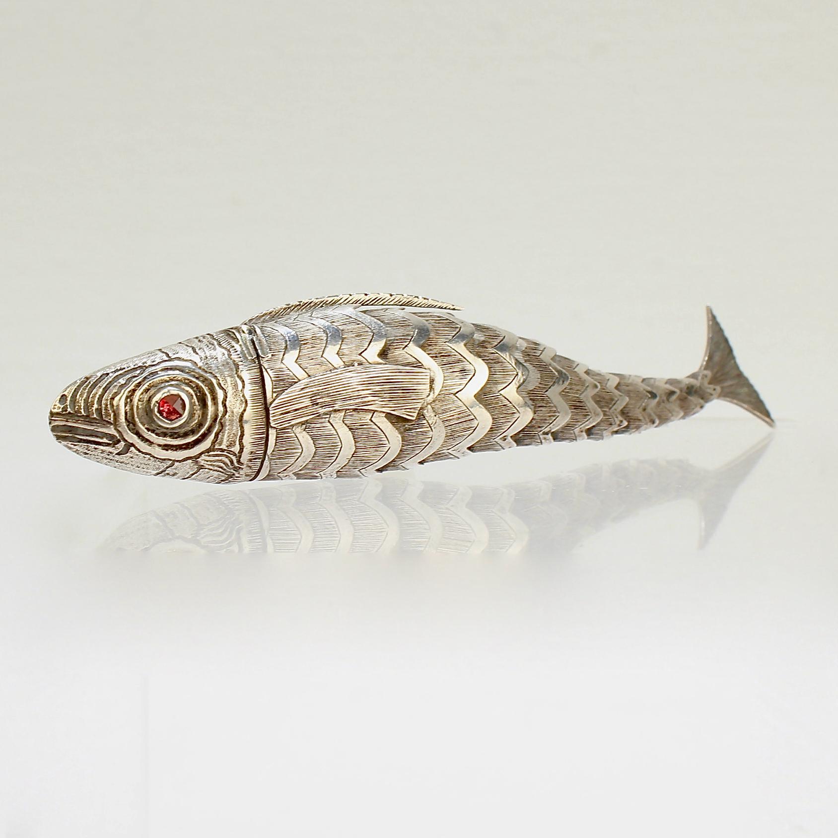 A very fine antique solid silver figural vinaigrette.

In the form of a fish with faceted garnet gemstone eyes and engraved fins and scales.

A hinged cover in the form of the fish's head opens to reveal a sponge compartment. The body supports 10