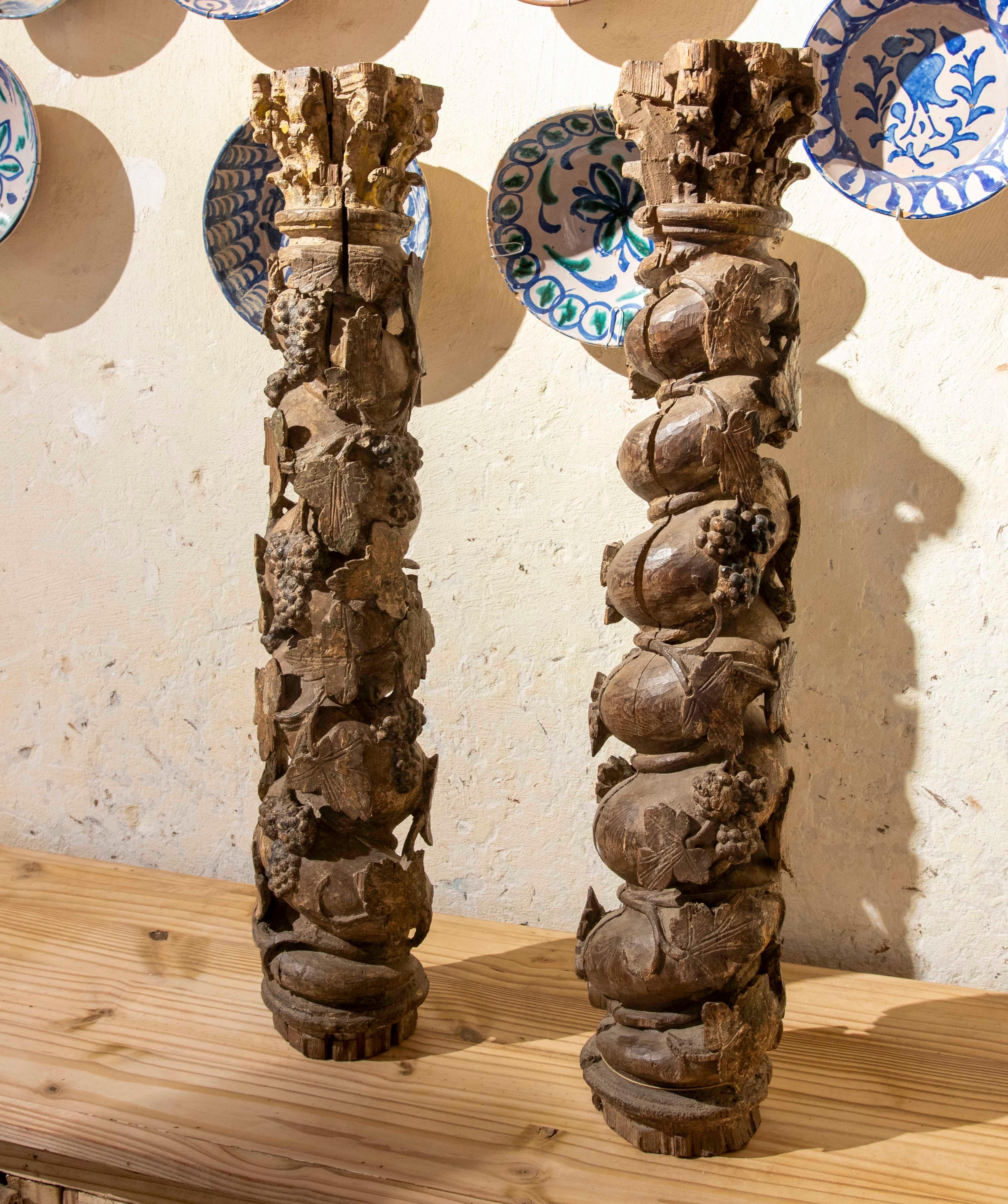 Una splendida coppia di colonne decorative realizzate in legno antico intagliato a mano. Ogni colonna presenta un elaborato disegno in rilievo con motivi di frutta e foglie, che evidenziano grappoli d'uva, melograni e fogliame, in uno stile che