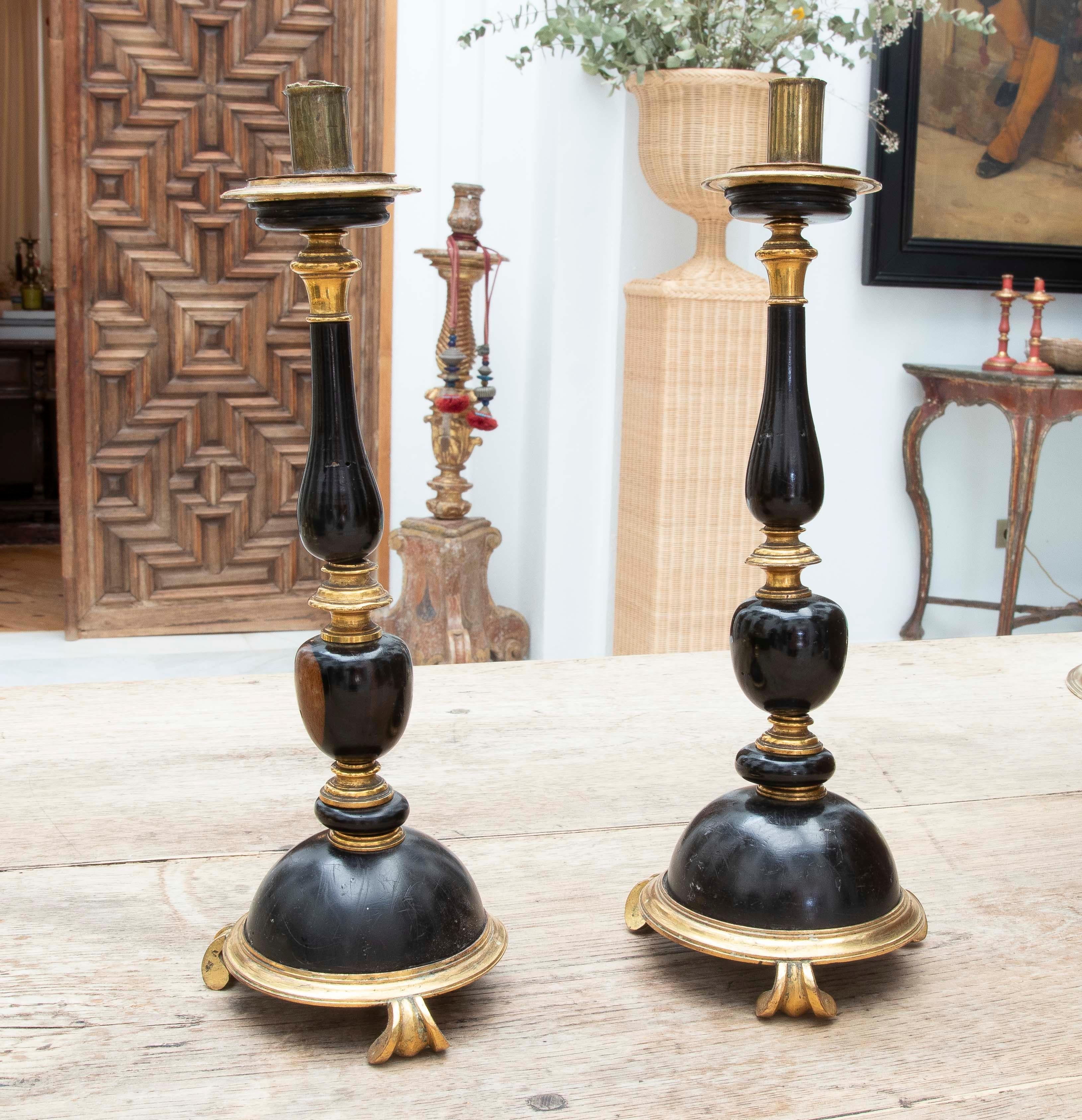 An impressive pair of altar or table candlesticks made of turned and carved wood, lacquered in deep black with gilt bronze details. The design is in keeping with the 18th-century historicist style, evoking architectural forms and liturgical