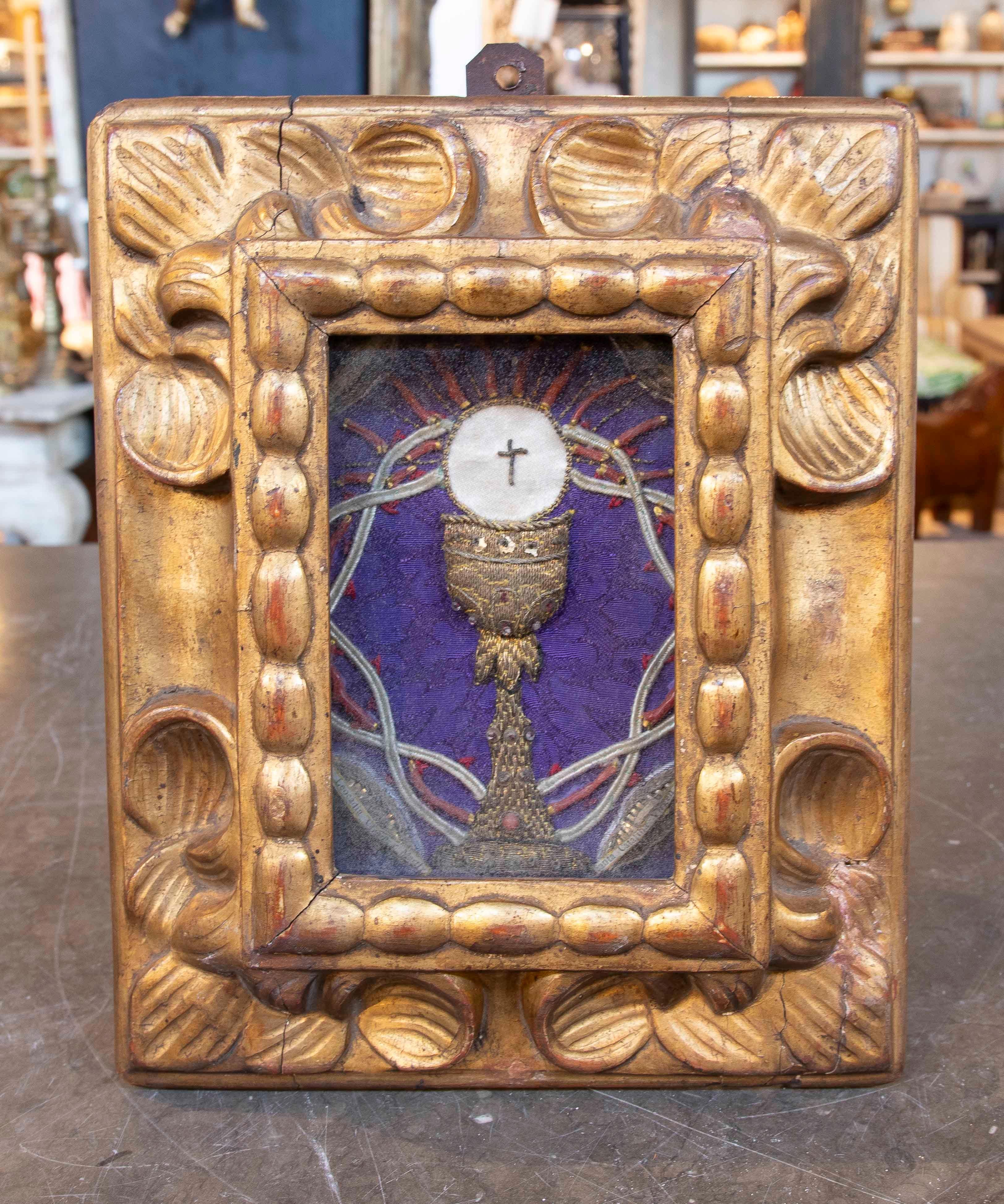 Un reliquaire religieux ancien avec une représentation symbolique de l'Eucharistie, comprenant un calice en or avec une hostie consacrée au sommet, orné d'une croix au centre. La pièce est encadrée dans un cadre en bois sculpté et doré avec des