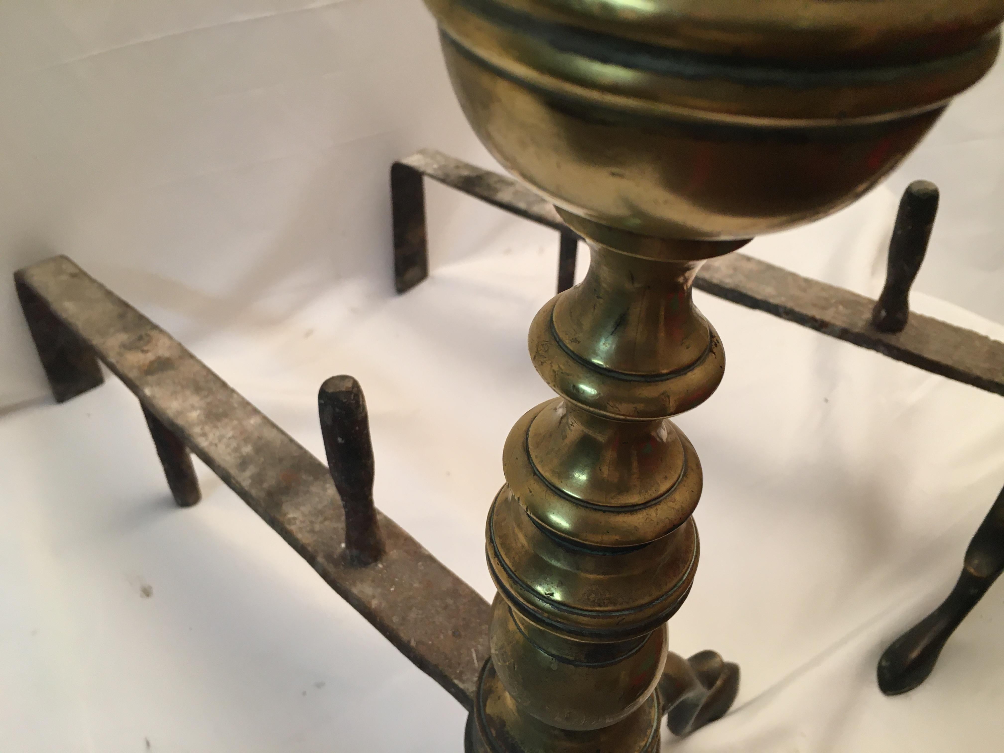 This handsome pair of fine brass Early American Chippendale andirons feature multiple turnings topped with a cannon ball style crown. The graceful spurred legs terminate on slipper feet. Sturdy log stops on the firedogs keep wood from slipping off. 