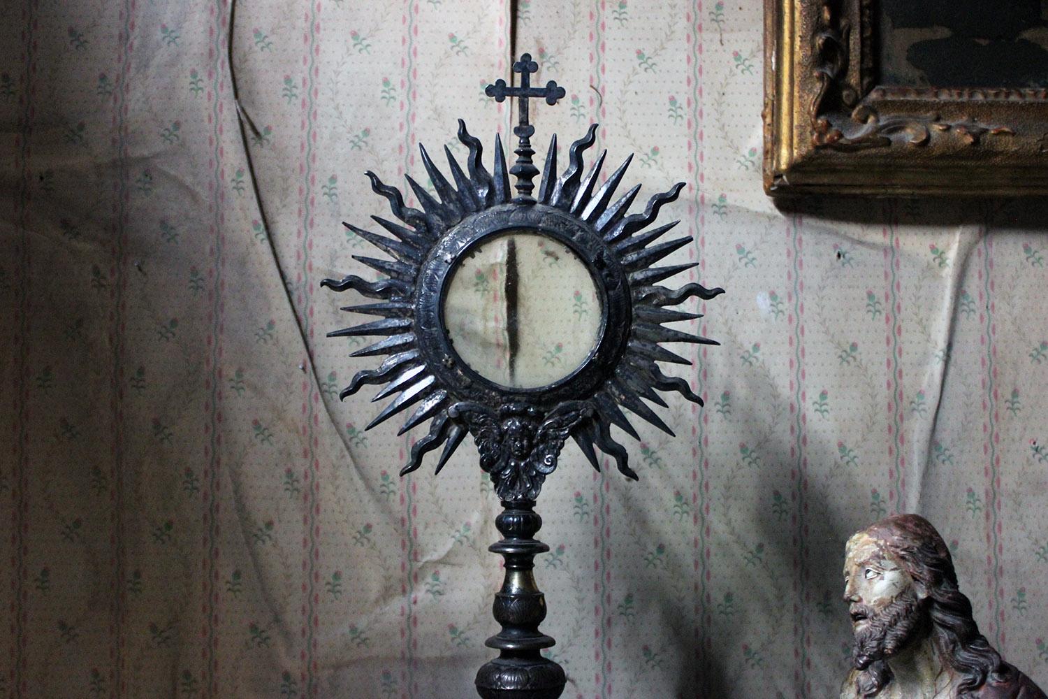 The beautifully crafted ostensory or monstrance, for the display of relics or objects of piety, the upper section as a sunburst with cross finial, the circular glass compartment opening to reveal a vacant interior, over a winged cherub to a turned
