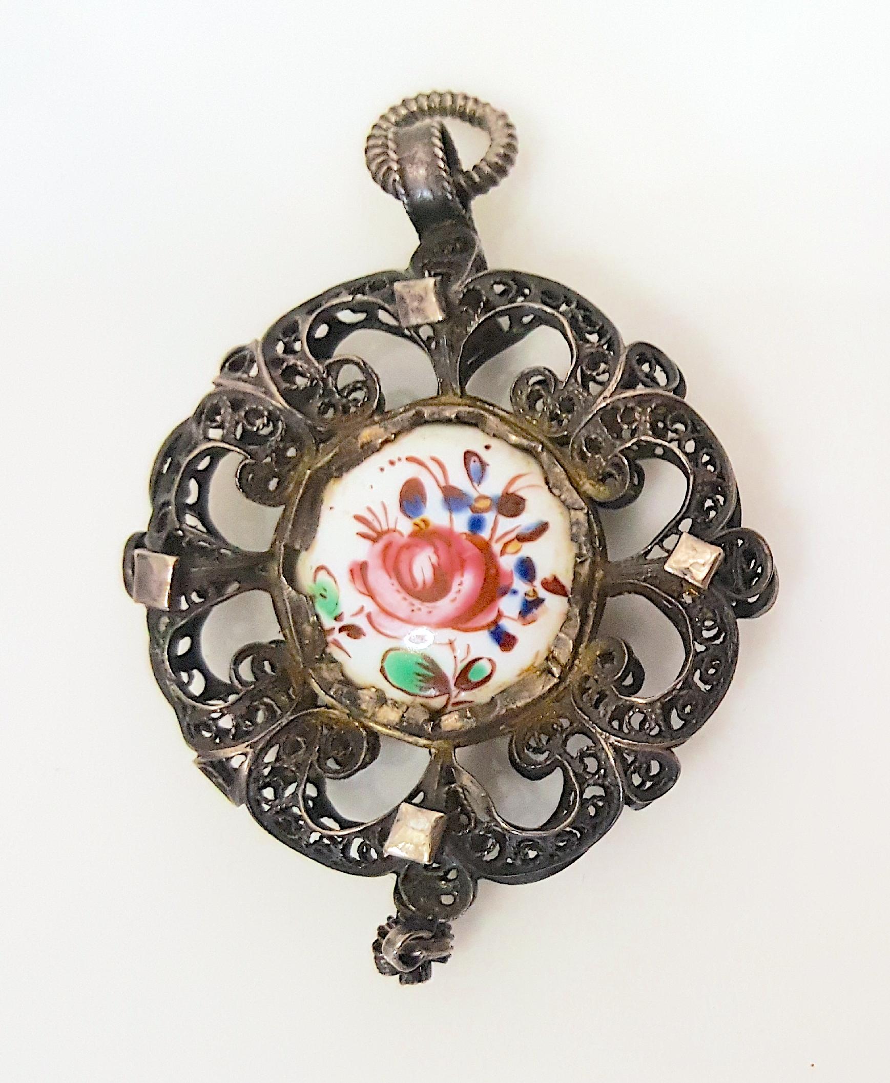 This early 18th-Century Spanish Rococo period silver-filigree double-sided pendant with dangle features miniature colorful enamel devotional paintings on both sides of a white porcelain centerpiece, which are associated with an April birth.

One