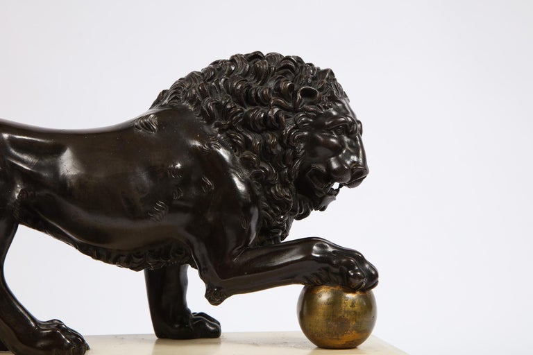 A beautiful 19th century neoclassical Grand Tour patinated and gilt bronze model of the Medici Lion, standing on a Carrara and griotte marble plinth. With magnificent form, the patinated dark brown lion is seen keeping one paw on a gilt ball. The