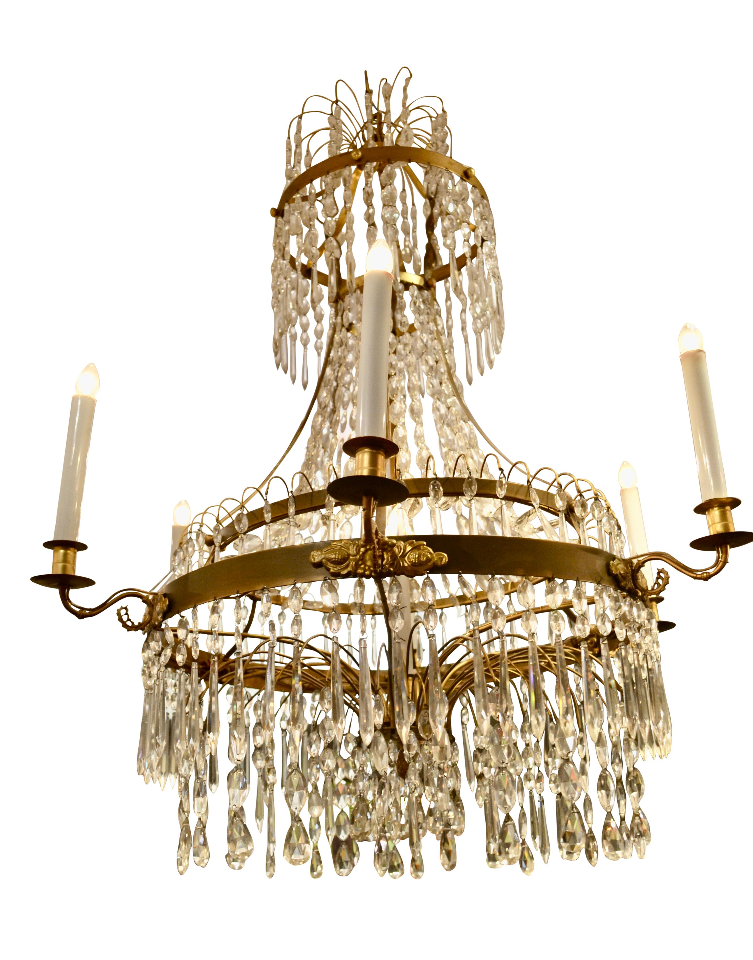 A neoclassic cut crystal chandelier, the three circular brass frames of differing dimensions are all hung with long cut crystals and almond shaped drops and chains. The bottom section features a spray of curved narrow brass rods which also support