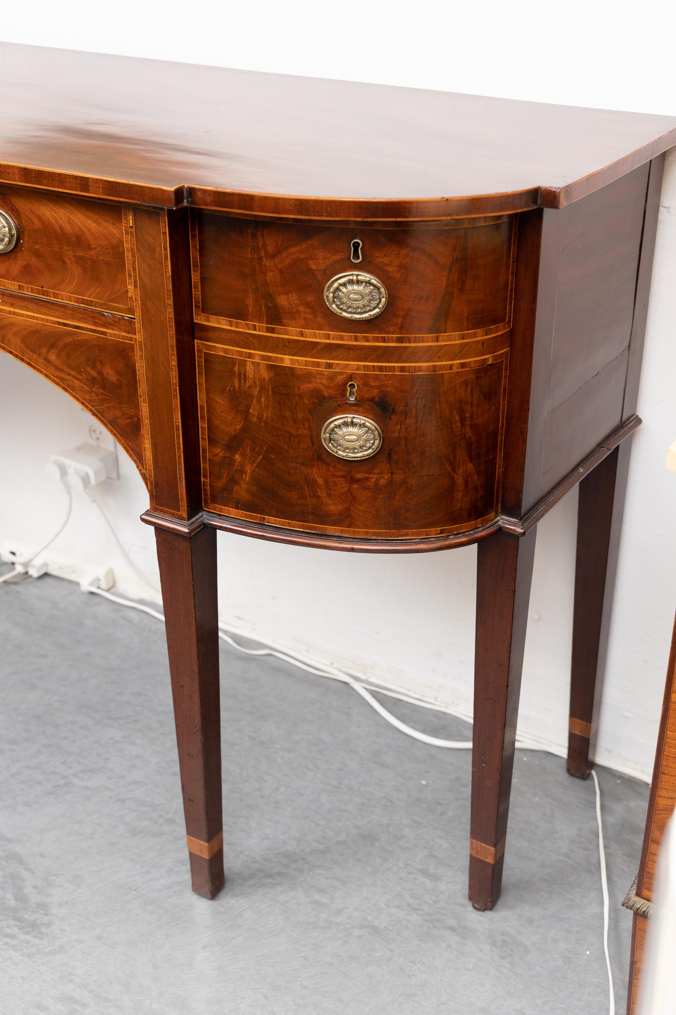 This is a graceful English George III style inlaid mahogany sideboard. The top has a straight edge over one large central drawer flanked by two curved double banks of drawers, all having figured mahogany and inlaid overall with rosewood crossbanding