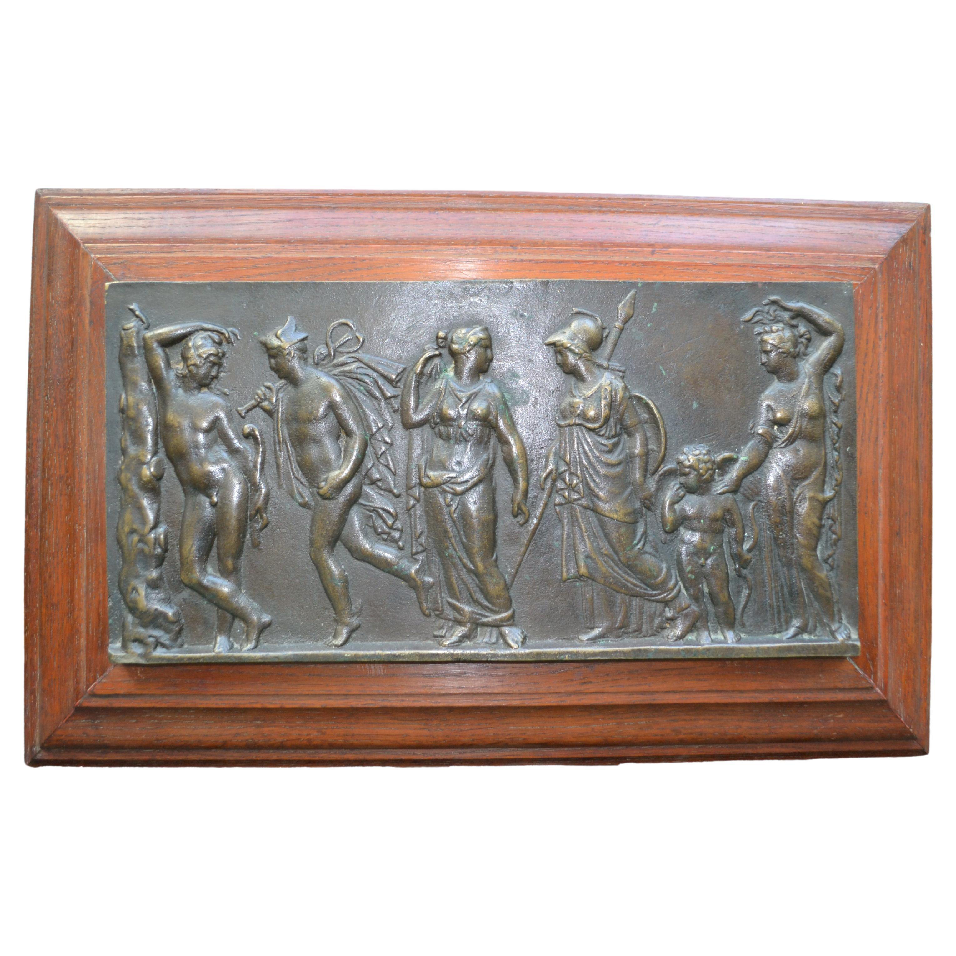 A Grand Tour heavy bronze bas-relief of a classical scene showing a retinue of six figures consisting of two nude standing males and three classically draped maidens including Athena wearing her characteristic Corinthian Helmet . In between Athena 