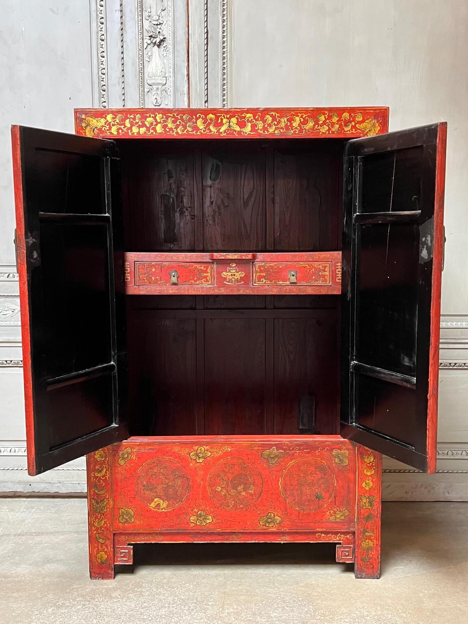 A very decorative red and black lacqured 19th century cabinet from Shanxi China. This cabinet has gilded decoration depicting mountain, foliage and temples with people as well as butterflies. It was probably originally used as a wardrope cabinet and