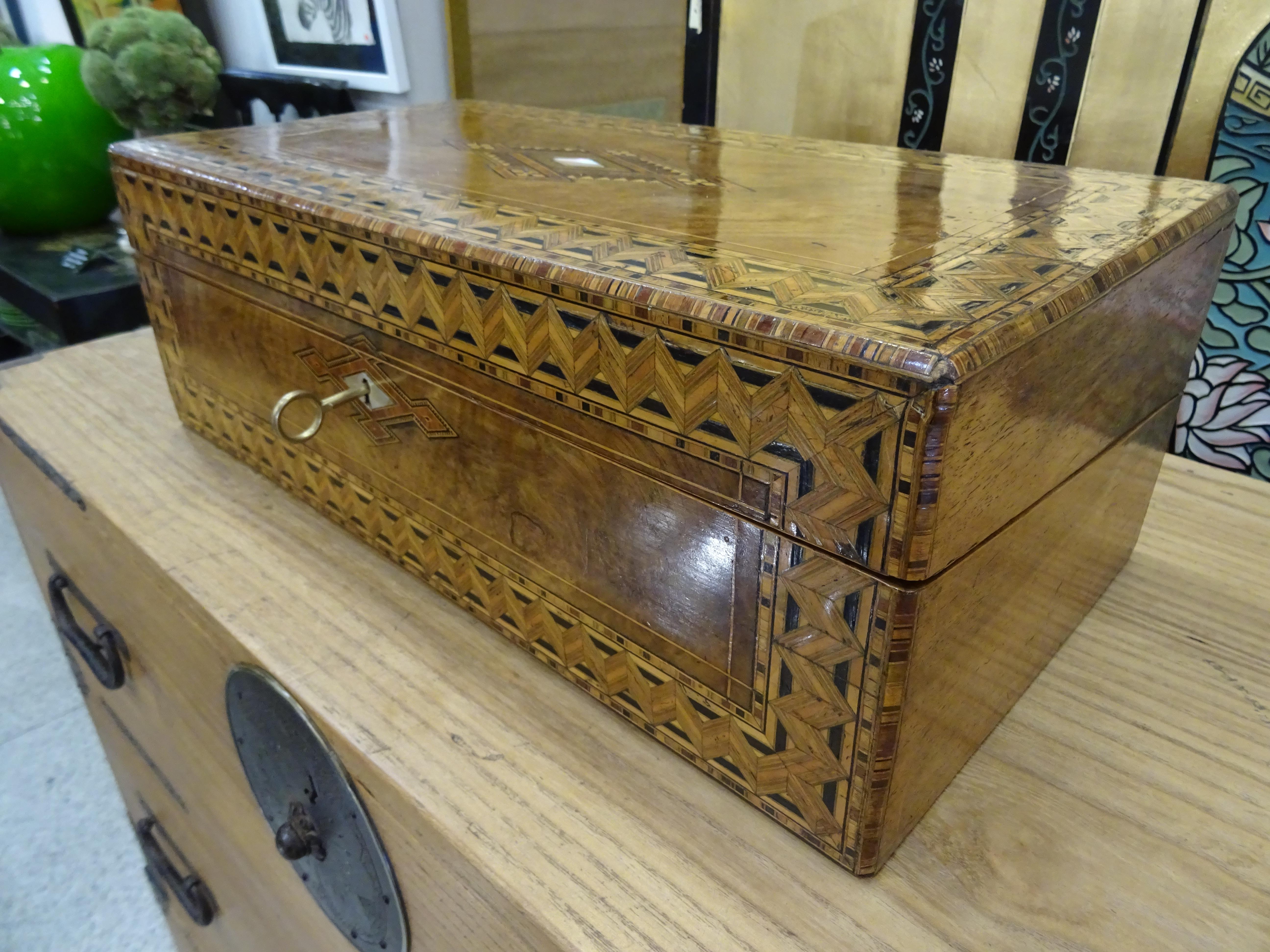 Amazing and refined English boat desk- box, inlaid wood with a geometric design and mother of pearl inlaid.
It opens and has different spaces for different desktop objects as well as the writing board. It has a key and it’s in a very good
