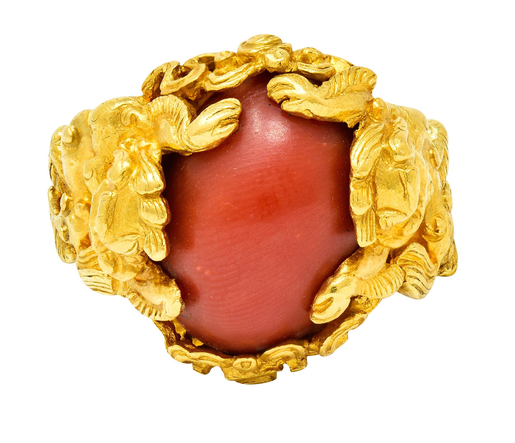 Ring is highly rendered to depict two dancing Fu dogs accompanied by scrolling whiplash

Centering an oval cabochon of coral measuring approximately 15.0 x 11.0 mm

Opaque with uniform orangey red color with good polish

Tested as 22 karat