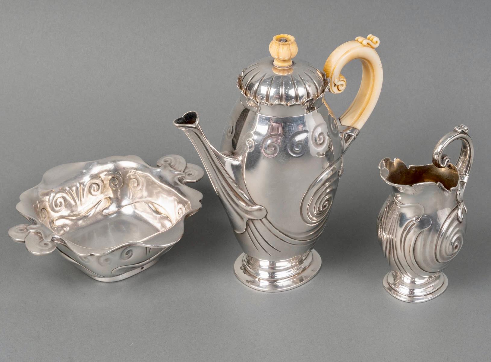 Juego de Té/Café Art Nouveau de plata de ley y marfil creado en 1900. Expuesto en la Exposición Universal de 1900.
Todas las piezas están estampadas y firmadas.

Servicio incluido:
- una cafetera/tetera de 21,5 cm de altura
- una jarra de leche de