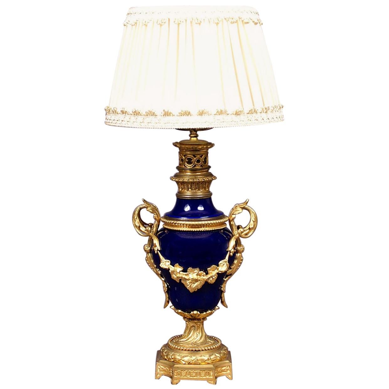 1900 cobalt porcelain and gilded bronze table lamp
Table lamp, square base with chamfered corners, engraved with leaf patterns, with eight legs. Above, a wider, porcelain belly, narrowed upwards, with gilded bronze decorations in the form of plant