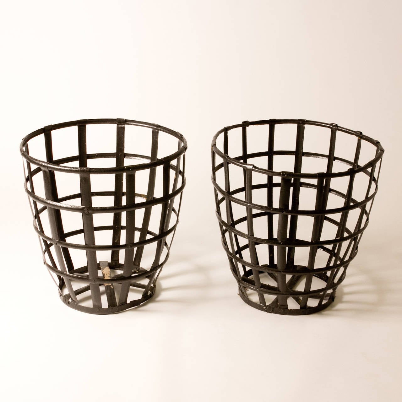 Pair of metal cage-style baskets containing two large blown-glass bottles, one green and the other clear. A beautiful piece of industrial design from turn-of-the-century France, these would work well in a garden, or as part of a table-scape or