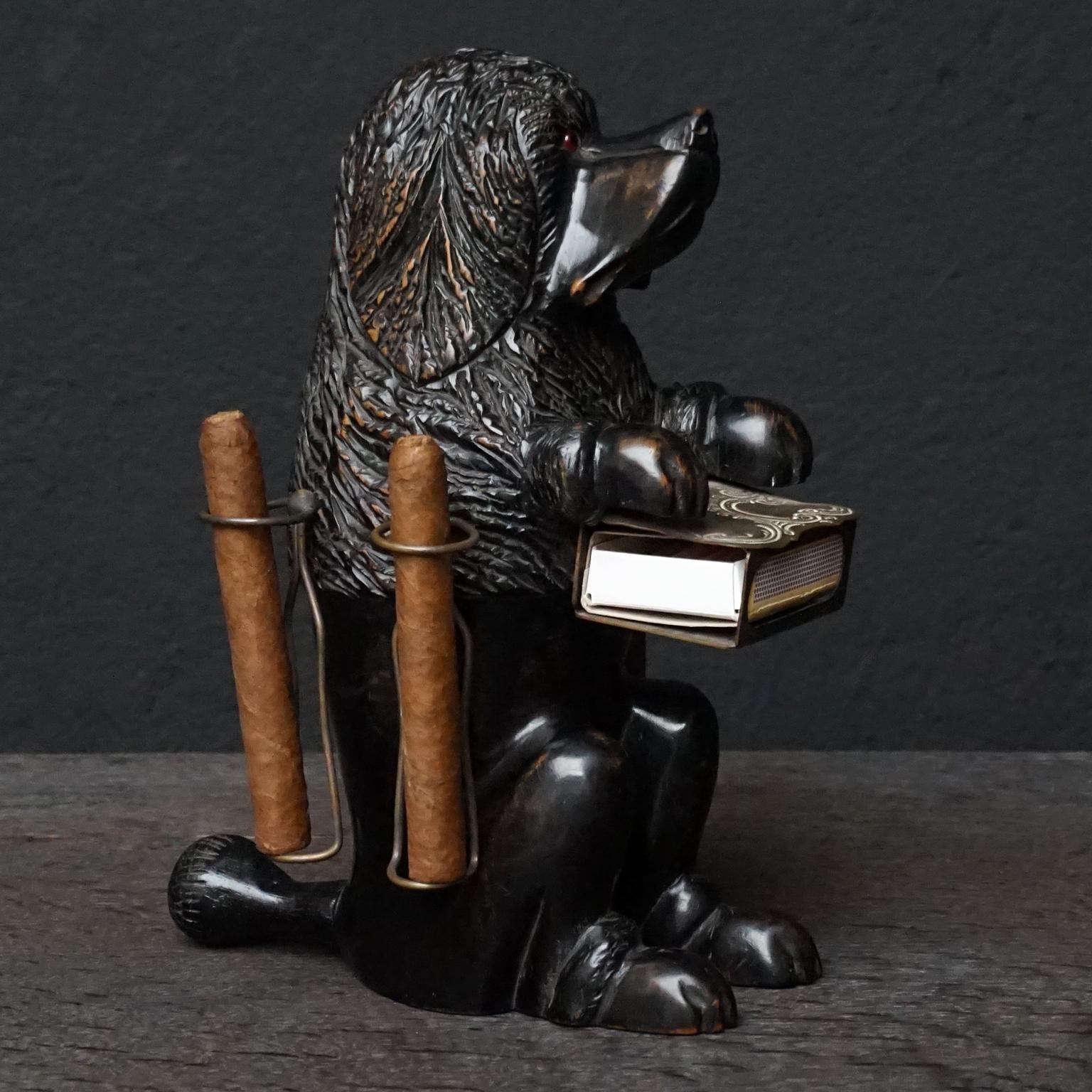 Swiss Brienz black forest hand carved linden wood begging poodle with brass matchbox holder and four brass cigar holders.

Black Forest wood carved art originates from a small mountain town Brienz, Switzerland. 
In the 19th century travelling became