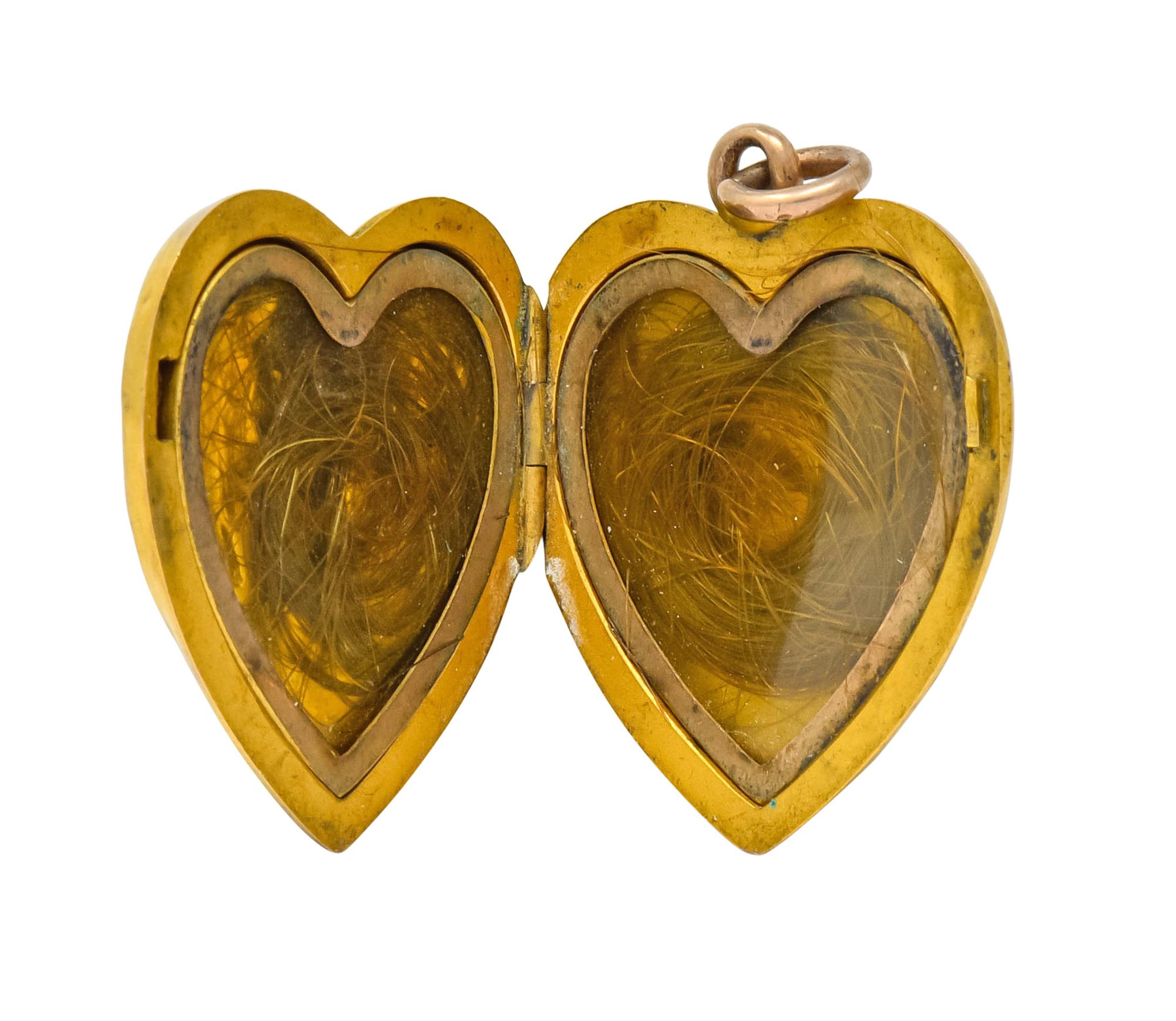 Heart shaped locket depicting a raised angelic face with corkscrew curls flanked by highly rendered angel wings

Opens on a hinge to reveal two covered recesses, each containing circular locks of hair

Completed by jump ring bale and matte gold
