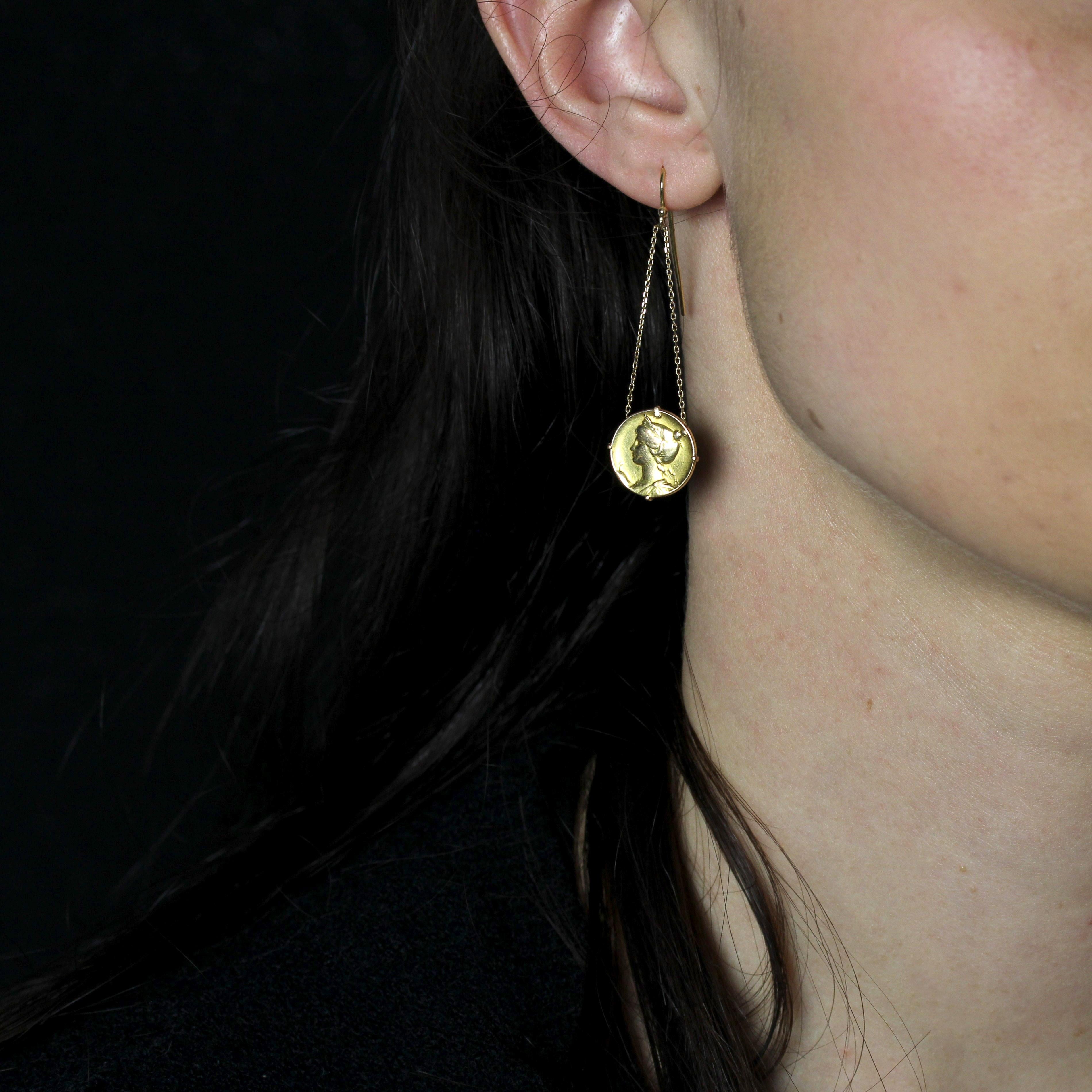 Pour les oreilles percées.
Boucles d'oreilles en or jaune 18 carats.
Chaque boucle d'oreille en or jaune est formée d'un crochet en col de cygne supportant deux fines chaînes limées-forçat, chacune retenant une petite médaille gravée d'un motif