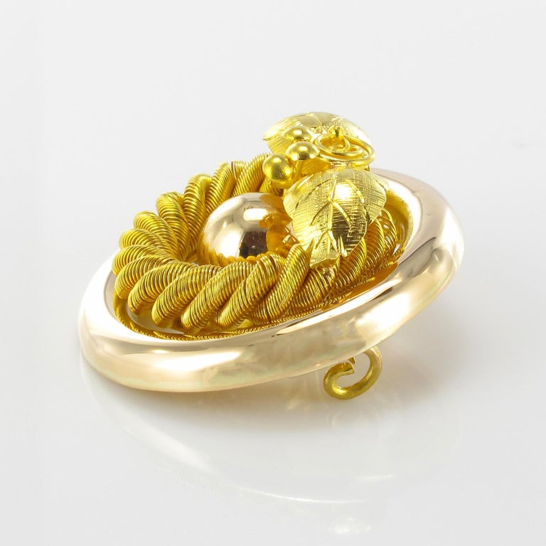 Brooch in 18 karat yellow gold.
This charming antique brooch of round shape is openwork and composed of a braid of gold wire topped by a decoration of vine leaves and bunch of grapes. In the center is a gold pearl. The clasp is a pin with