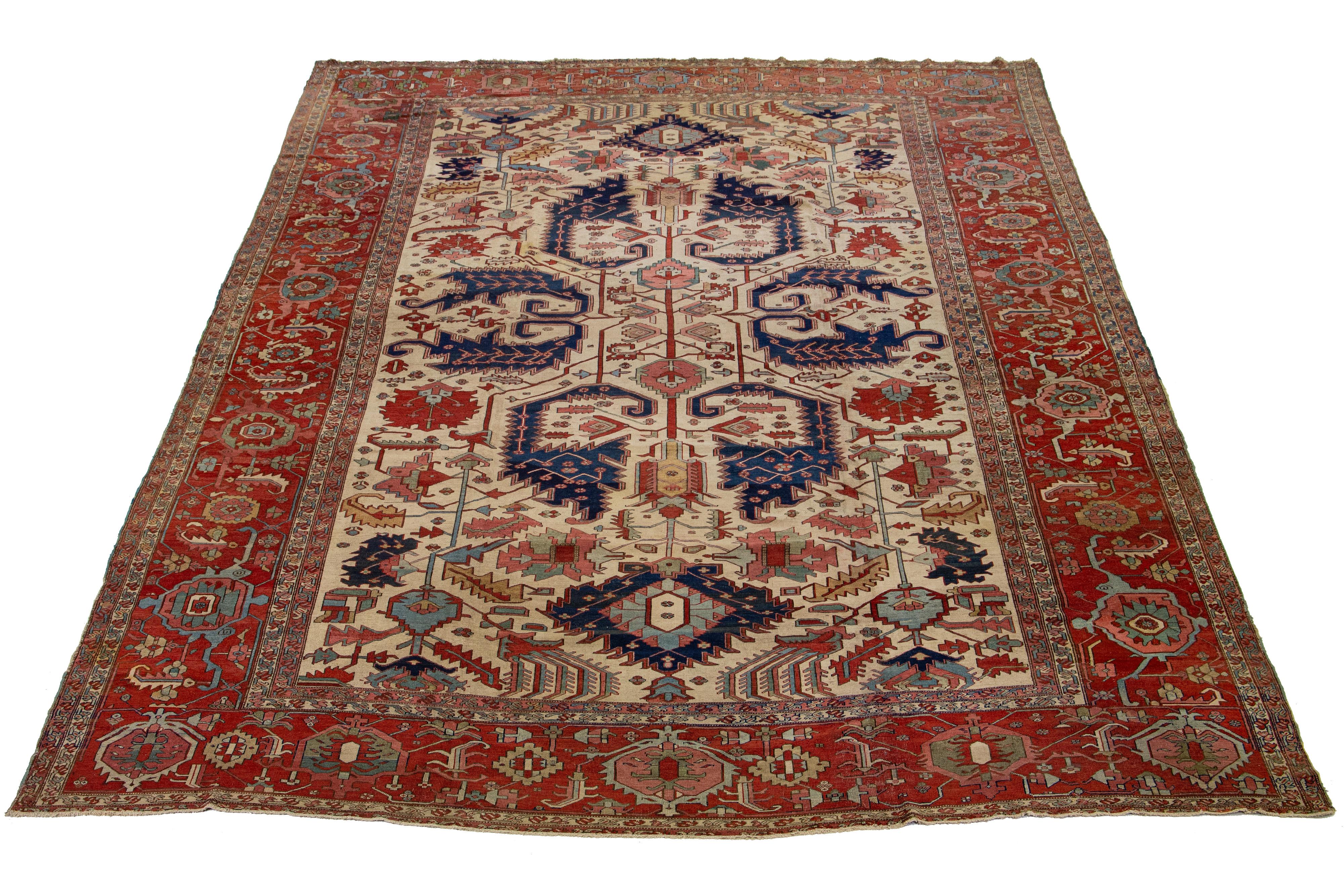 This large antique Persian Serapi rug is crafted from hand-knotted wool. The color field is a beige-tan shade that displays a captivating floral pattern embellished with various shades of color.

This rug measures 13'3