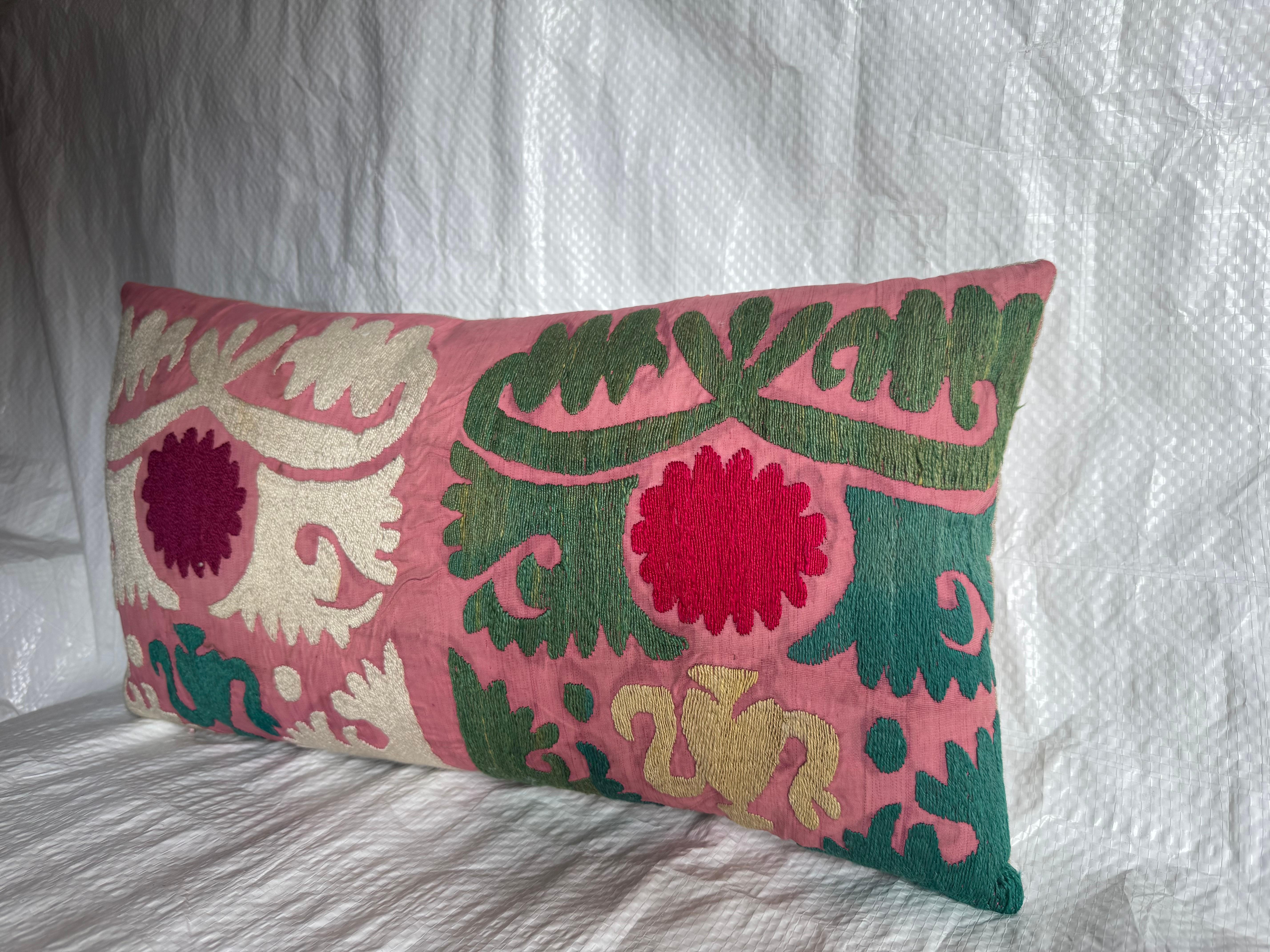 Un exquis coussin Suzani ancien, fabriqué en Asie centrale au début des années 1900. L'oreiller présente des médaillons floraux brodés à la main et des motifs de vigne stylisés en rouge, ivoire, vert et or sur un fond rose tendre.

Les textiles