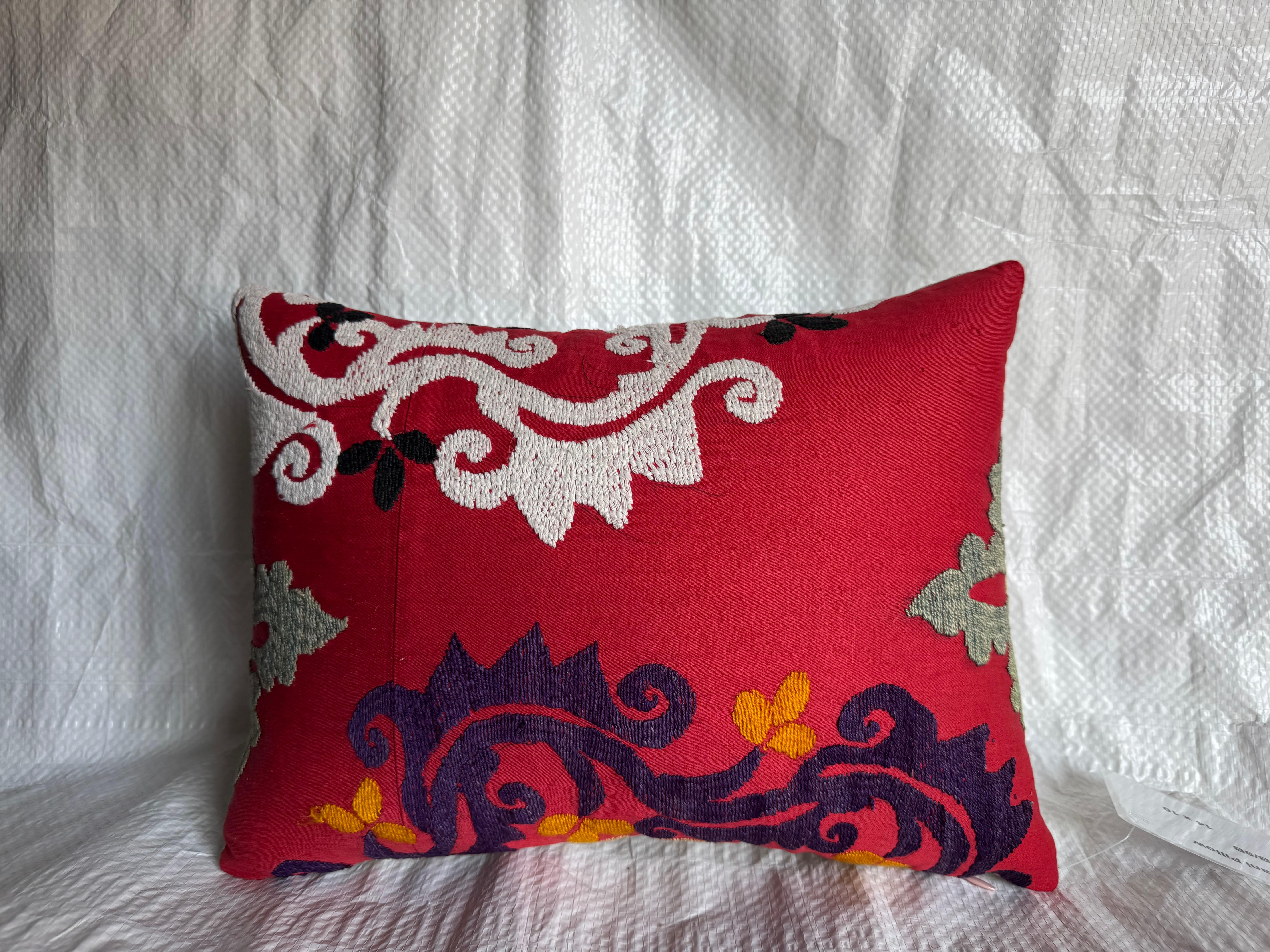 Un magnifique coussin Suzani antique datant du début des années 1900, brodé à la main en riches fils de coton sur une base rouge foncé. Le design présente des motifs floraux tourbillonnants de couleur crème, violette et jaune, exprimant l'art