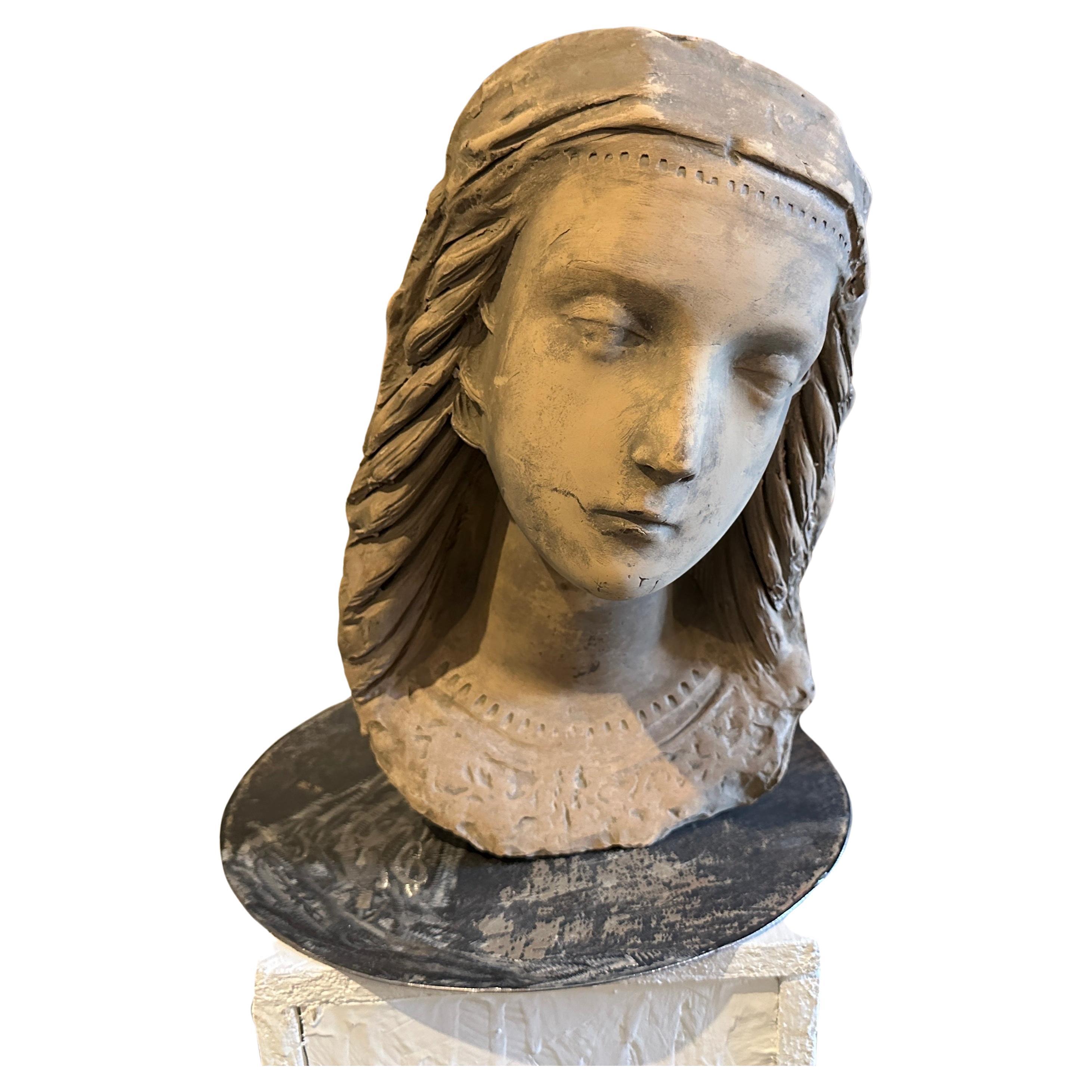 Cette tête de jeune femme en terre cuite sur un nouveau socle en fer est une œuvre d'art sculpturale saisissante, mêlant les formes organiques et les motifs stylisés caractéristiques du mouvement Art nouveau aux influences régionales distinctives de