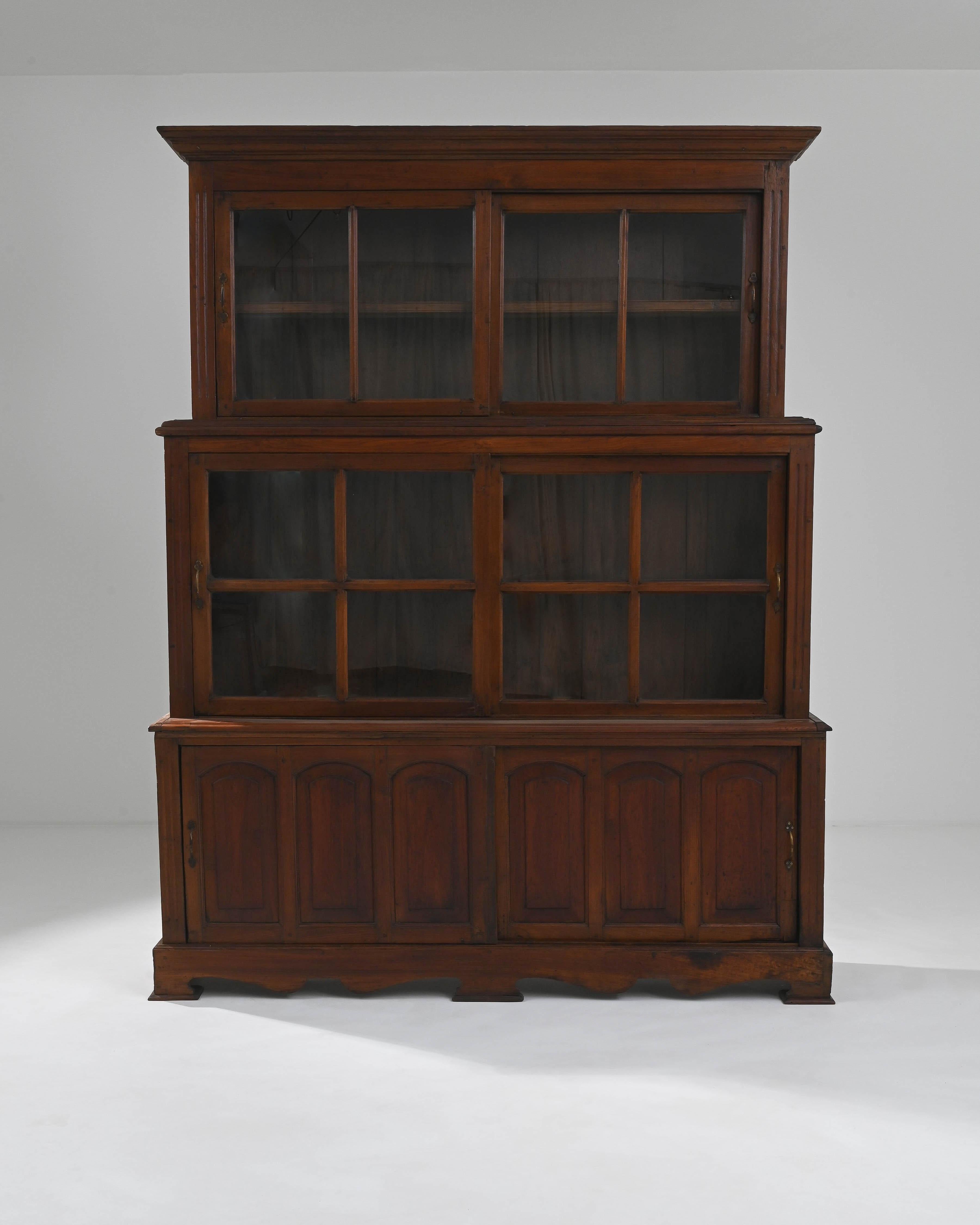 A wooden vitrine created in Asia circa 1900. This towerings display case is composed of three stacked levels of glass compartments. Sliding doors on each level allow access to the ample storage space within. The preserved original patina glows a