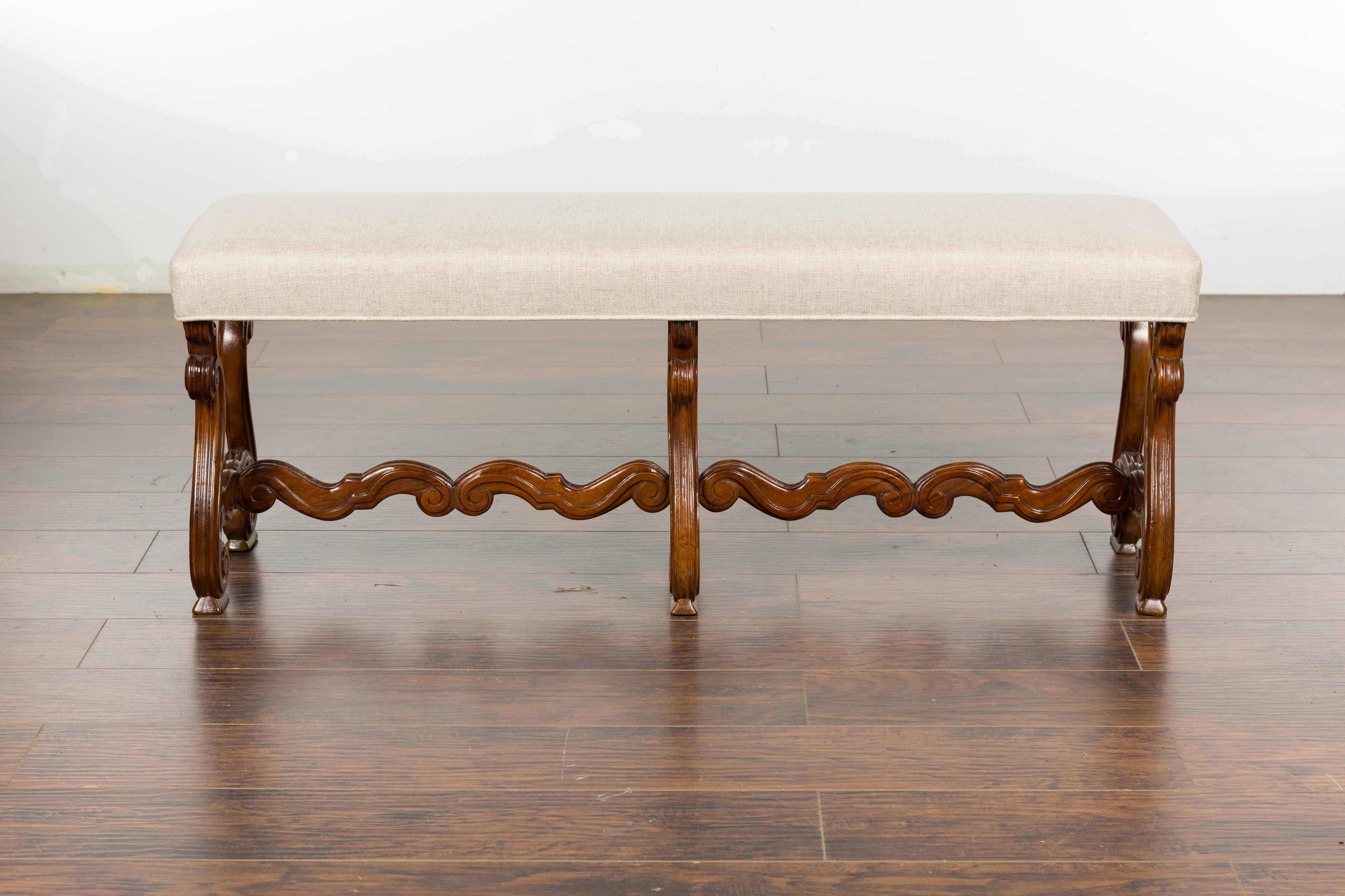 A French Baroque style walnut bench from circa 1900 with carved lyre-shaped legs and new linen upholstery. Incorporate the elegance of Baroque style into your living space with this stunning walnut bench from the early 20th century. Imbued with a