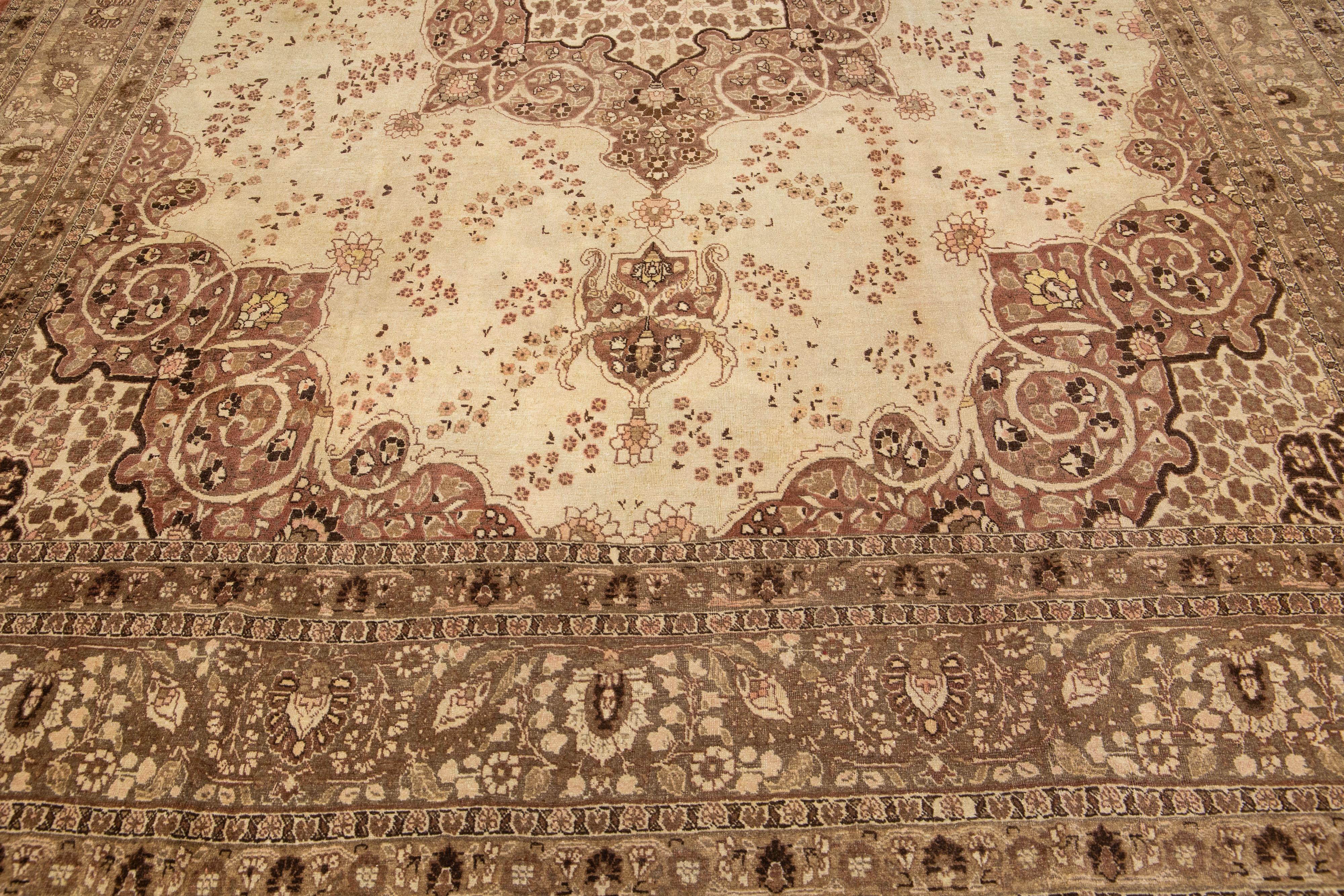 Cet exceptionnel tapis persan en laine Tabriz présente un exquis motif floral traditionnel en médaillon avec un accent pêche saisissant sur un fond beige et marron. Méticuleusement noué à la main, ce tapis ancien est un splendide chef-d'œuvre qui