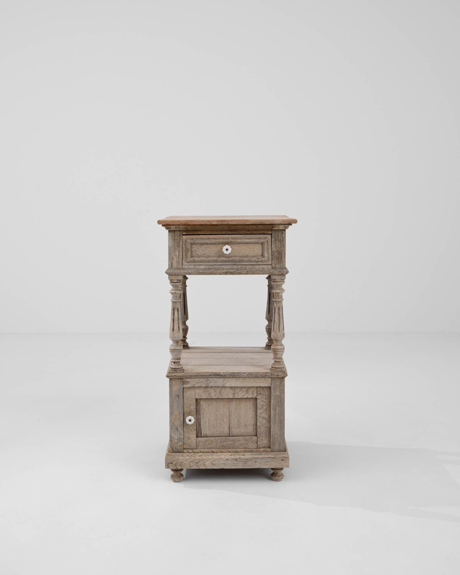This early 1900s Belgian Bleached Oak Bedside table epitomizes rustic charm and understated elegance. Crafted from the finest oak, its bleached finish highlights the natural grain and texture, invoking a sense of serene antiquity. The table features
