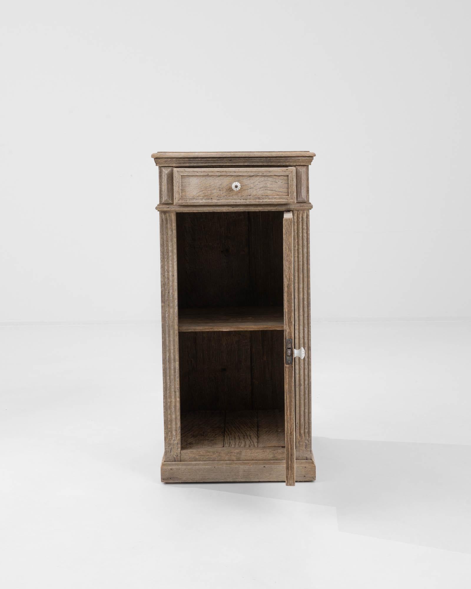 This is a 1900s Belgian Bleached Oak Bedside table that exudes antique charm and simplicity. The pale, sun-kissed finish accentuates the natural wood grain, giving this piece an airy feel that would brighten any bedroom. Its compact design features